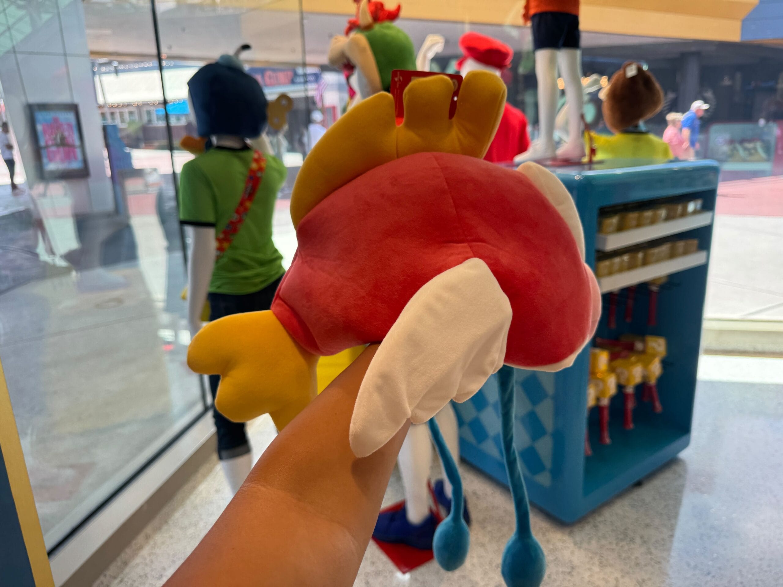 A person holds a Cheep Cheep Hat plush toy inside a Universal Studios store with mannequins in the background.