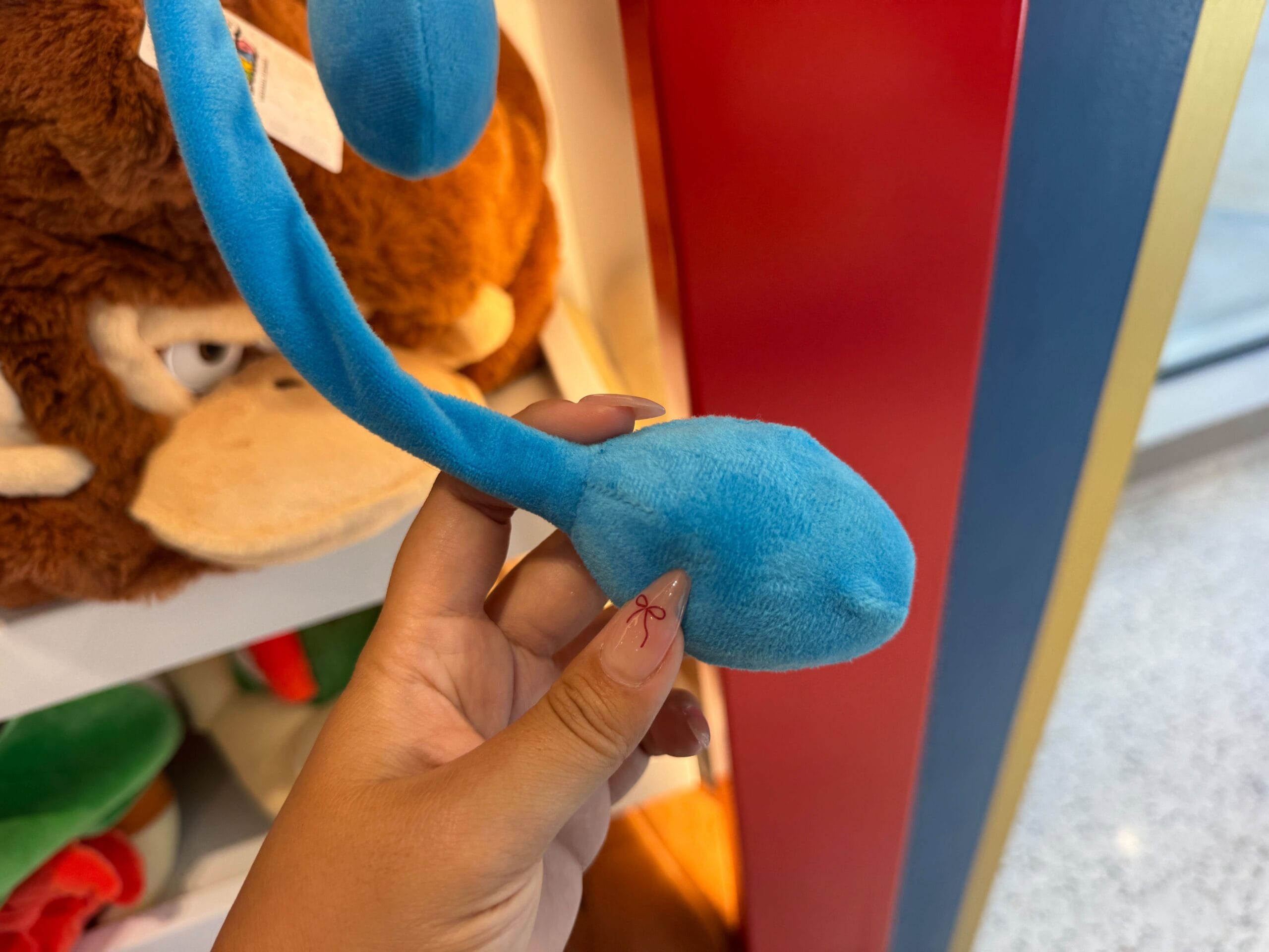A hand holding a blue plush toy tail in a store at Universal Studios, with other plush toys in the background.