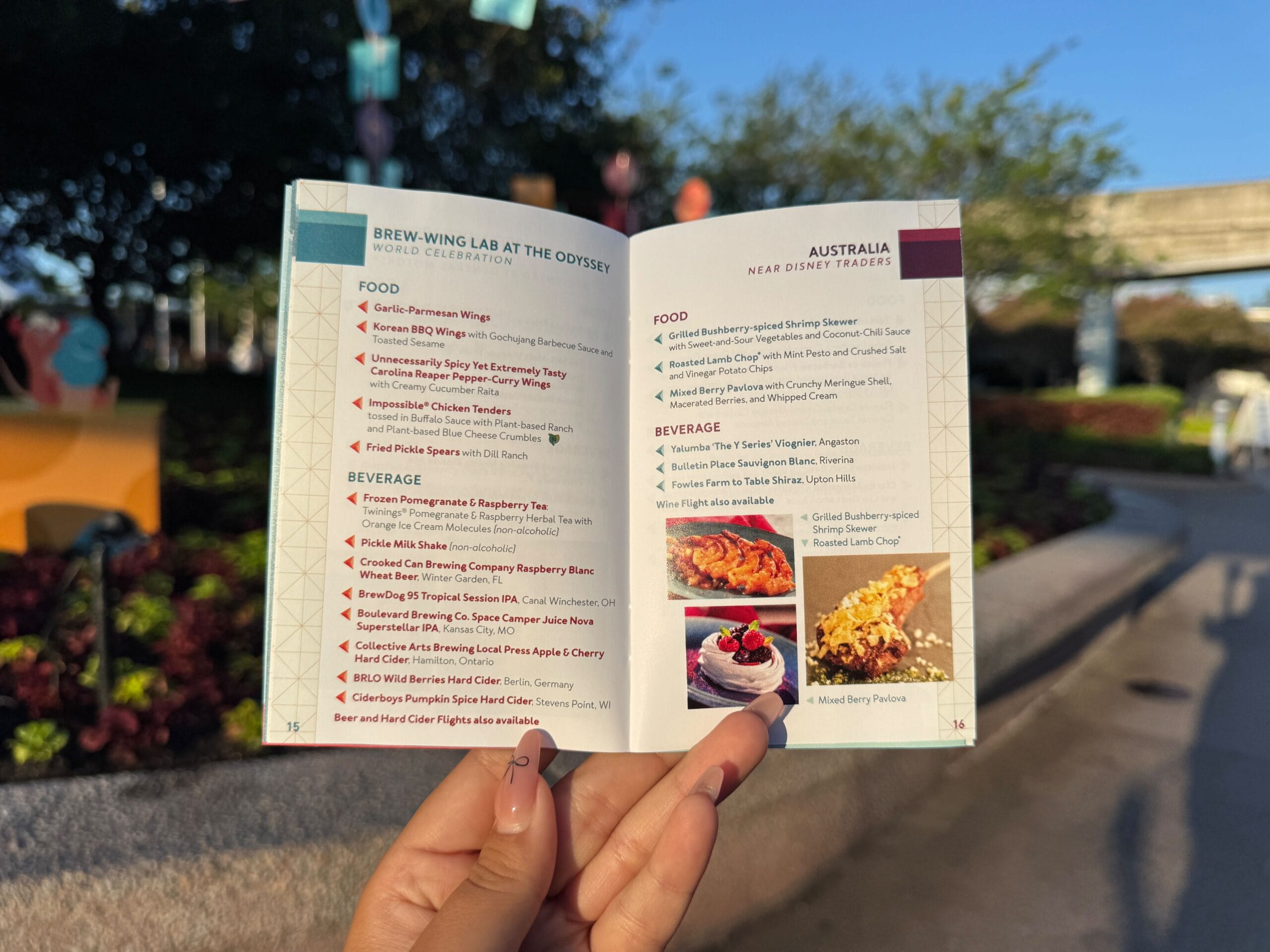 A hand holds an open event menu outdoors, showing food and beverage options for two locations.