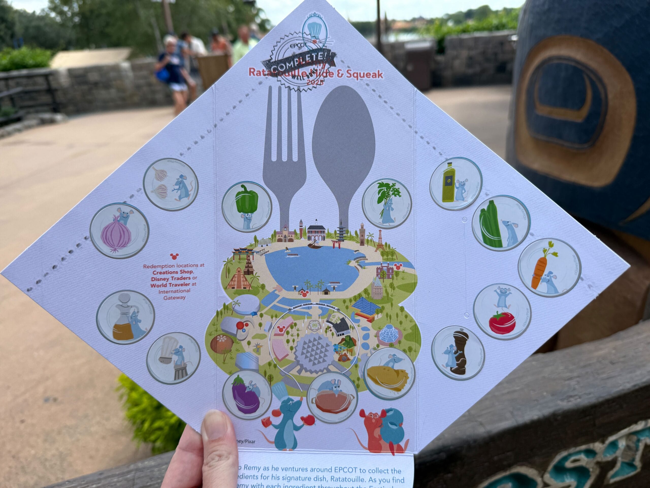 Hand holding a 2025 Remy's Ratatouille Hide & Squeak map at the EPCOT Food & Wine Festival, covered with stickers and food icons.