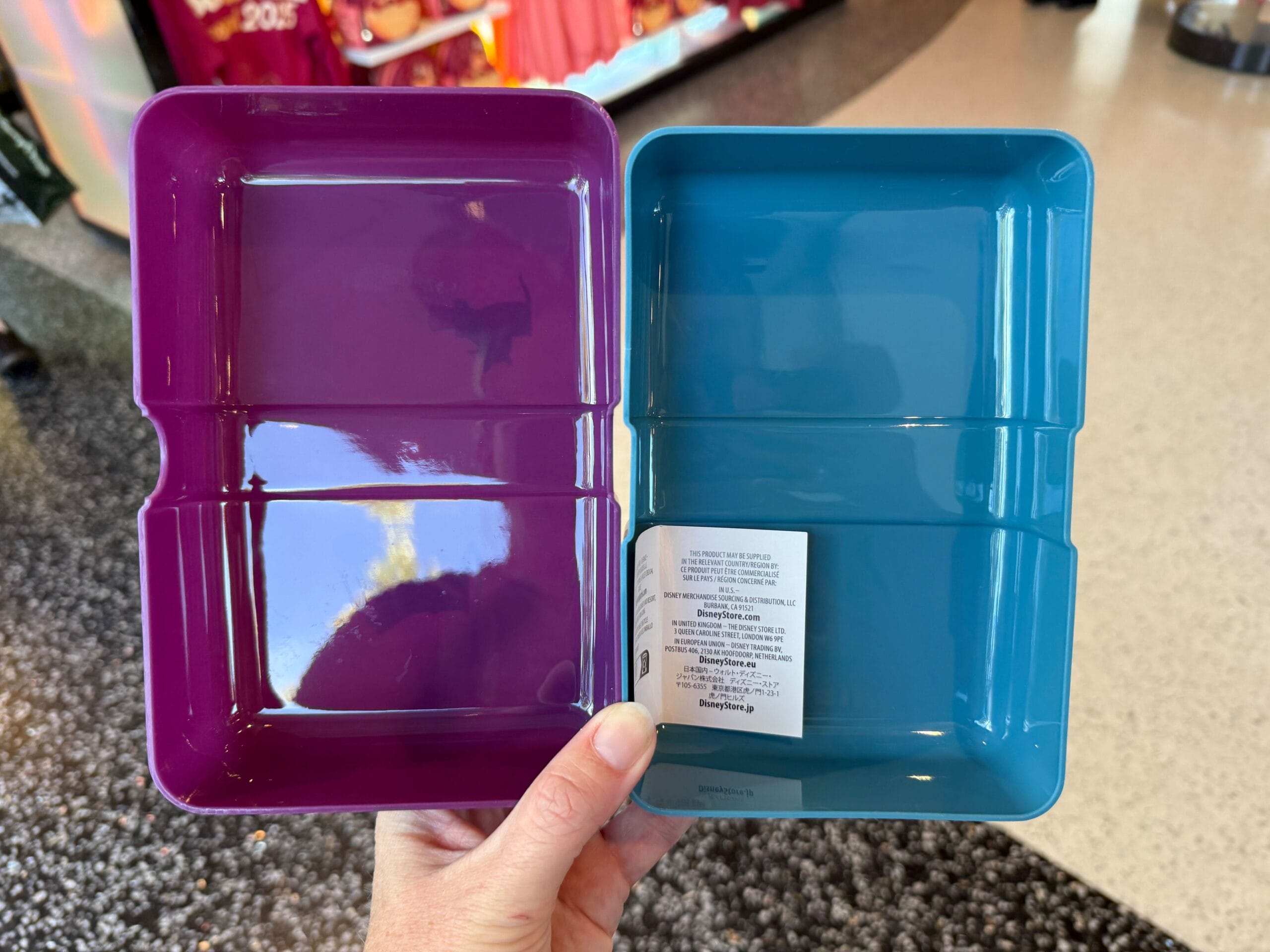 A hand holds two trays from Remy's Ratatouille Hide & Squeak at the 2025 EPCOT Food & Wine Festival.