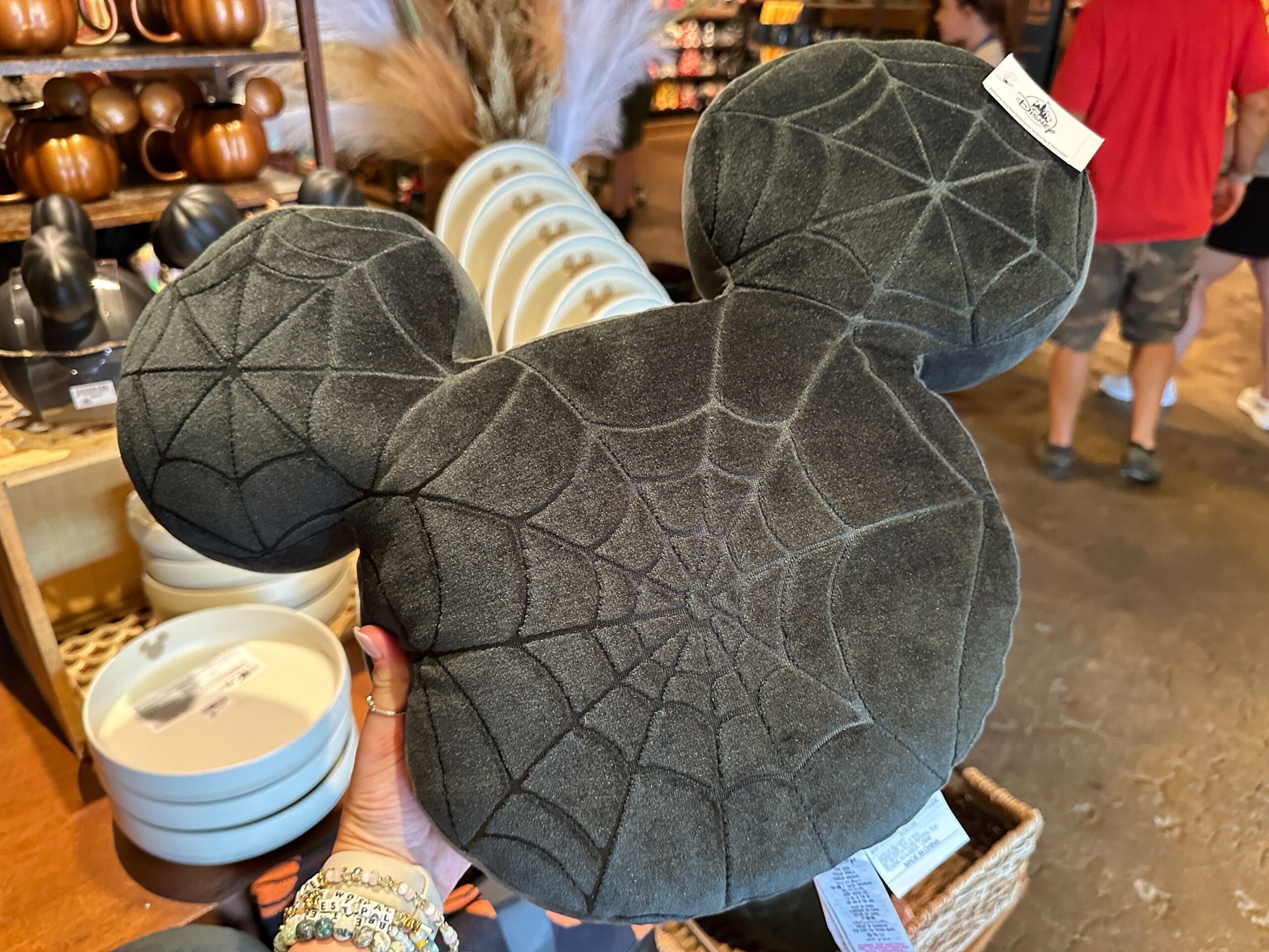 A hand holds a black Mickey Mouse-shaped pillow with a spiderweb pattern, perfect for Halloween Home Decor.