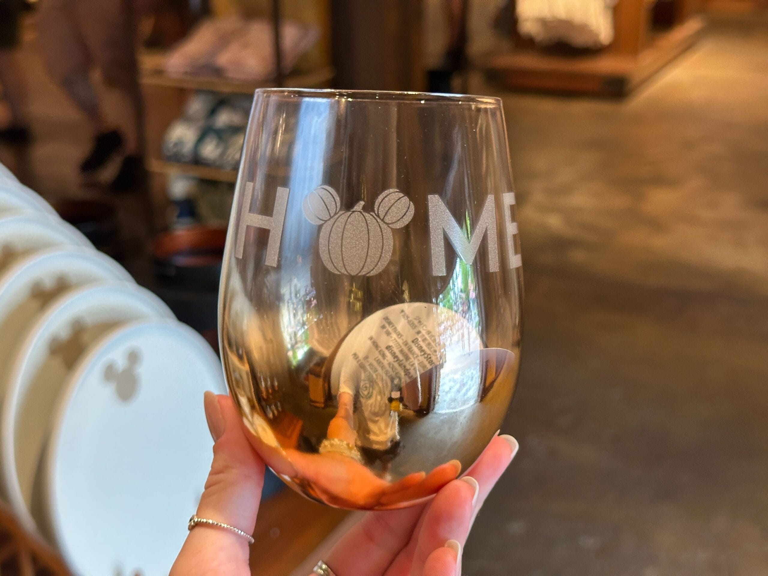 A hand holds a glass with "HOME" etched on it, the "O" as a Mickey Mouse head—perfect for your Halloween Home Decor.