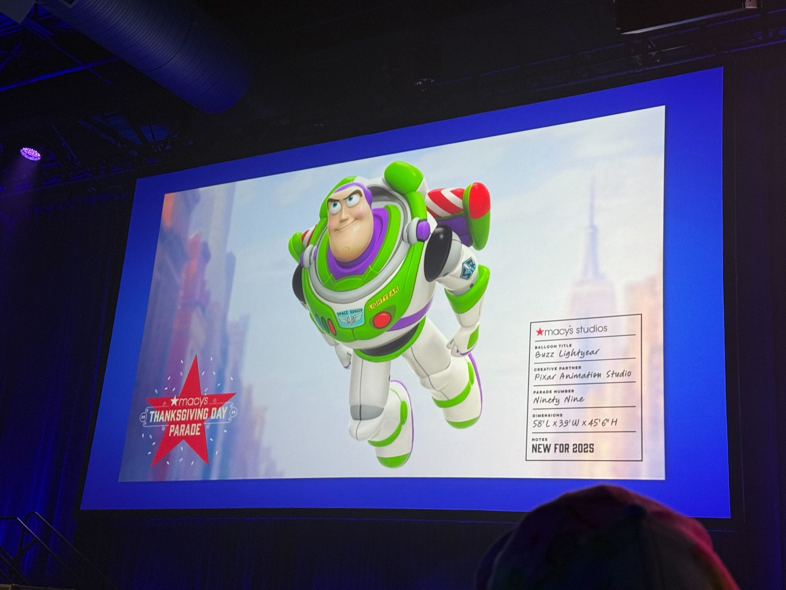 A screen displays Buzz Lightyear and details about his appearance in the Macy’s Thanksgiving Day Parade.
