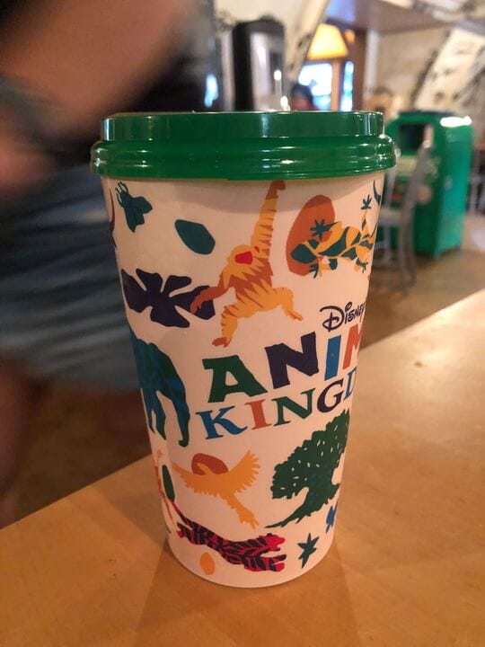 A Disney’s Animal Kingdom cup with colorful animal and plant illustrations sits on a wooden table indoors.
