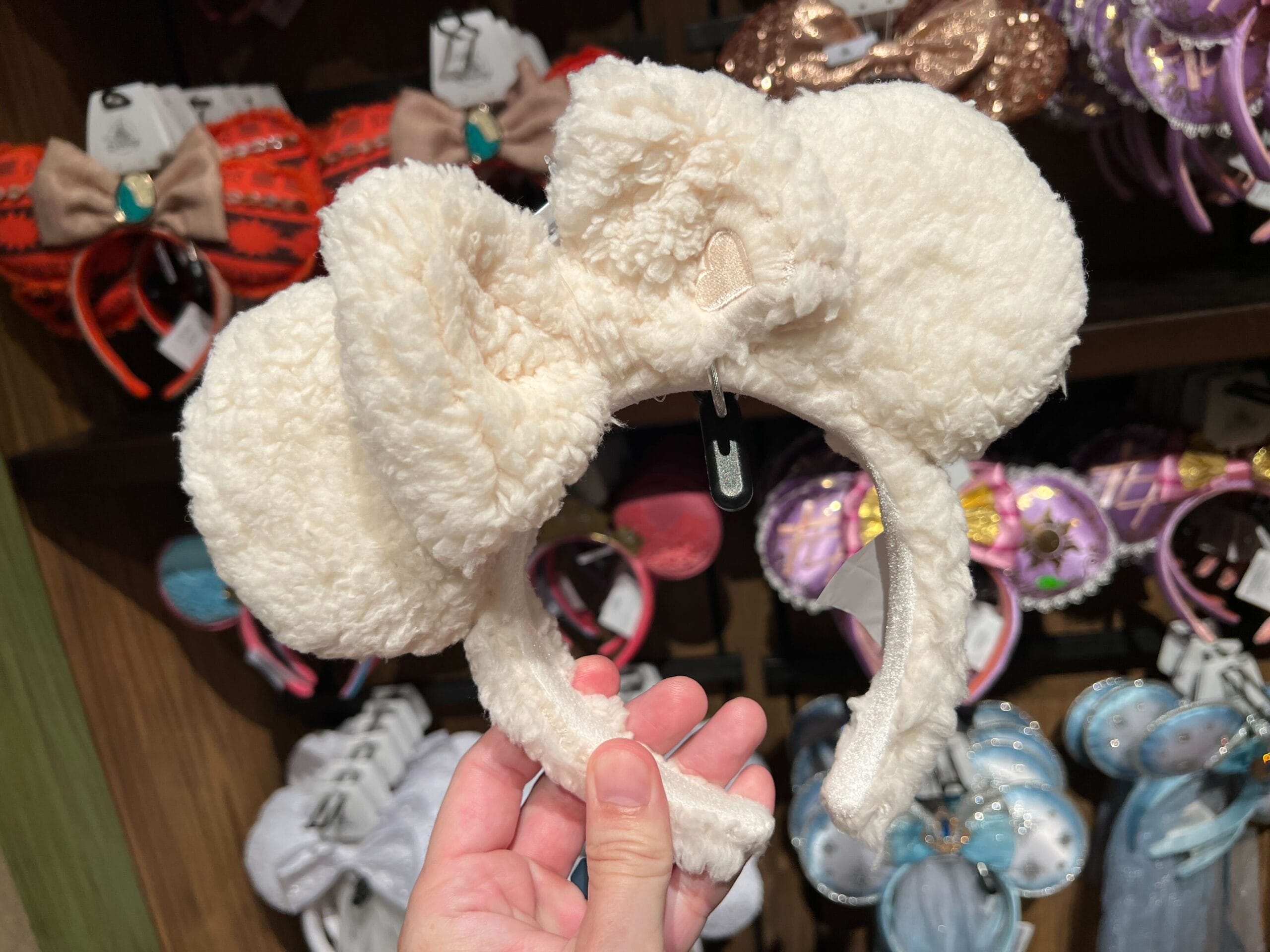 A hand holds a plush ear headband inspired by Minnie Mouse amid colorful options on store shelves.