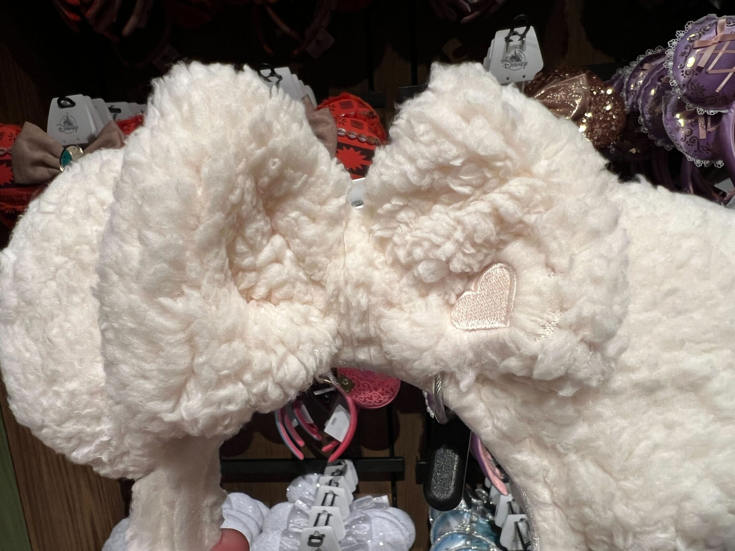 Close-up of a Plush Ear Headband with cute ears and heart detail, displayed among other headbands in a store.