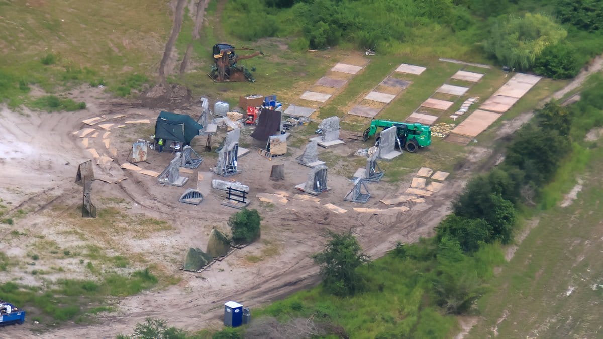 Aerial view of a construction site with equipment, scattered structures, and rectangular plots on grassy terrain.