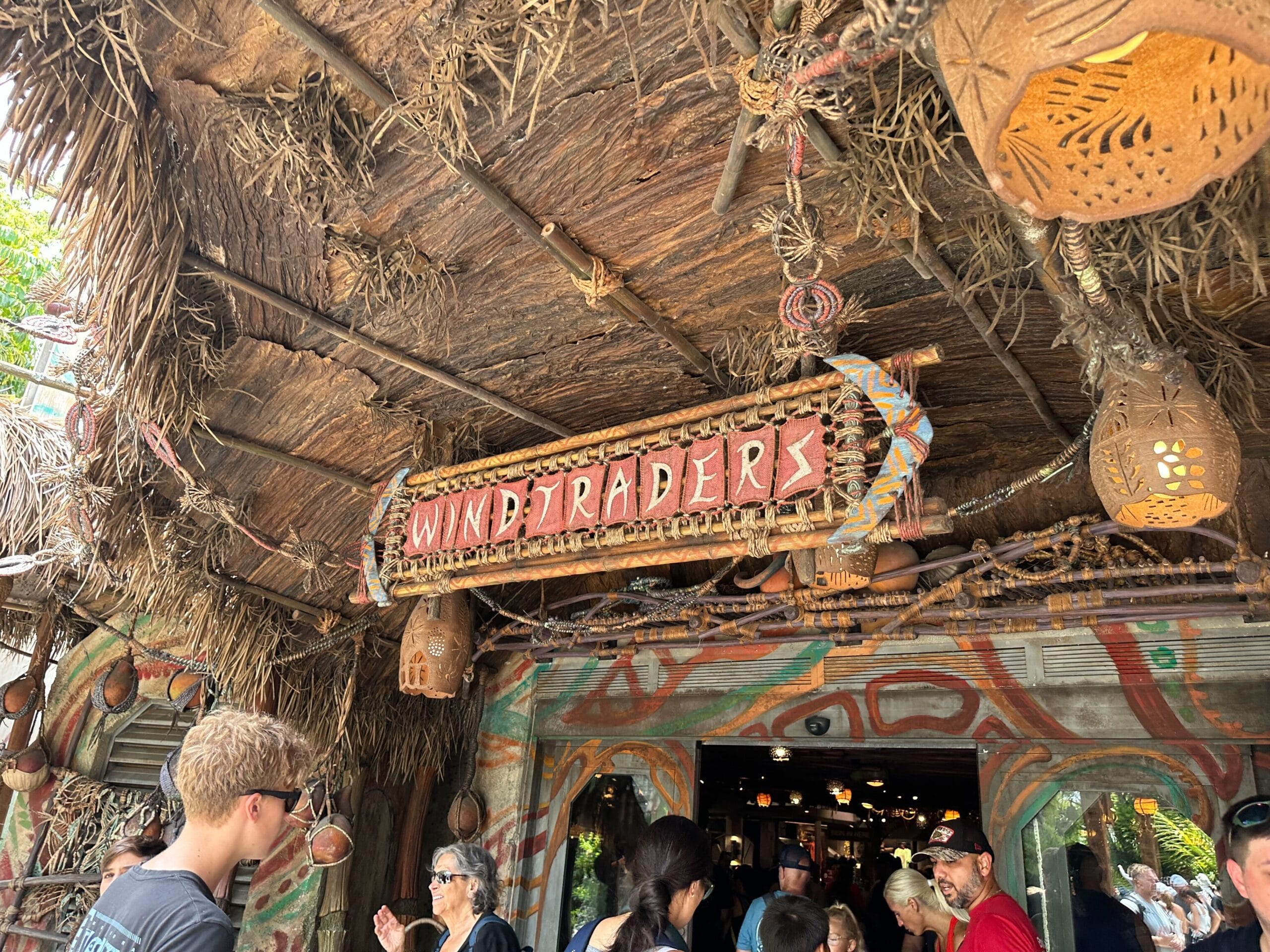 People stand outside the Windtraders store in Pandora, beneath a thatched roof and colorful hanging lanterns.