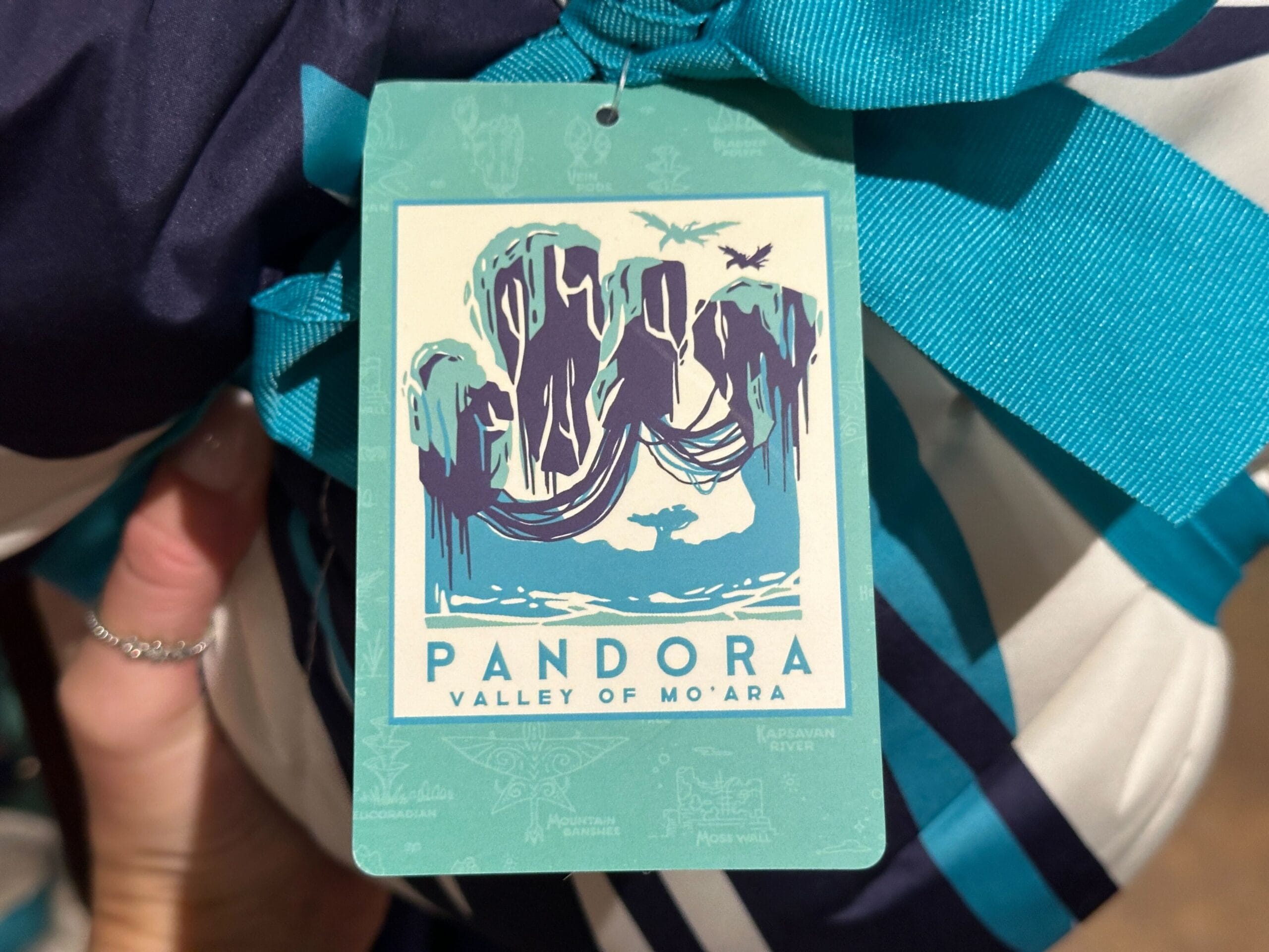 Tag featuring floating mountains and text "Pandora Valley of Mo'ara," perfect for Pandora Merch, tied with a blue ribbon.