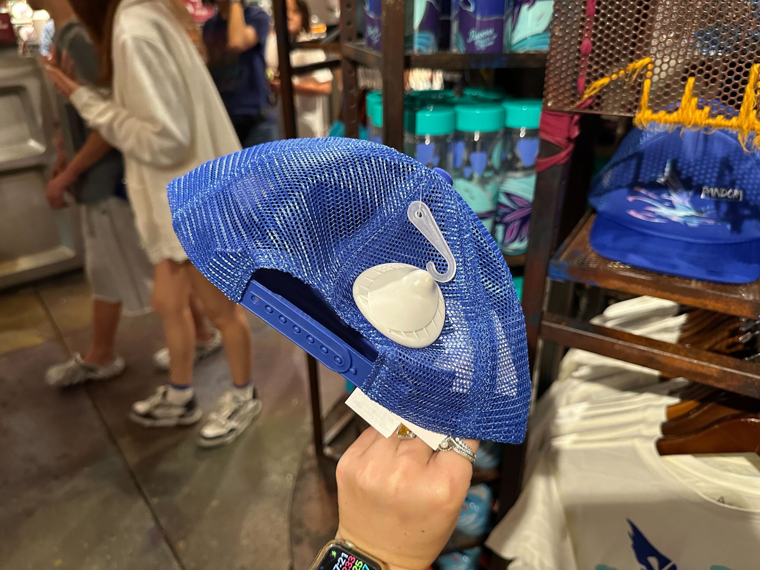 A person holds a blue mesh cap with Stitch’s ear from Disney’s Lilo & Stitch beside Pandora merchandise in a store display.