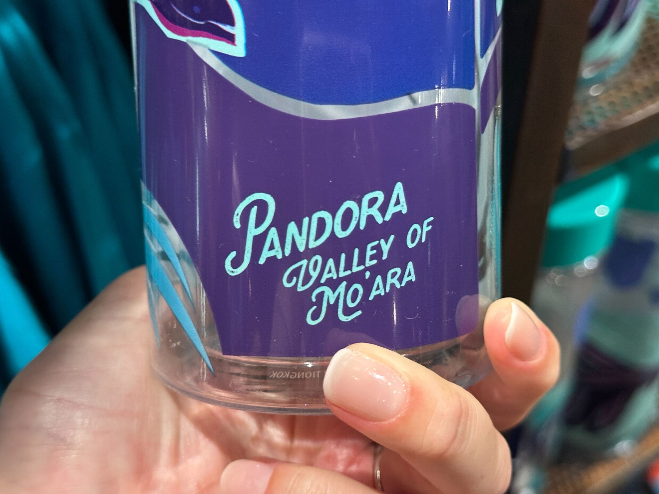 A hand holds a purple cup labeled "Pandora Valley of Mo'ara," a unique piece of Pandora Merch.