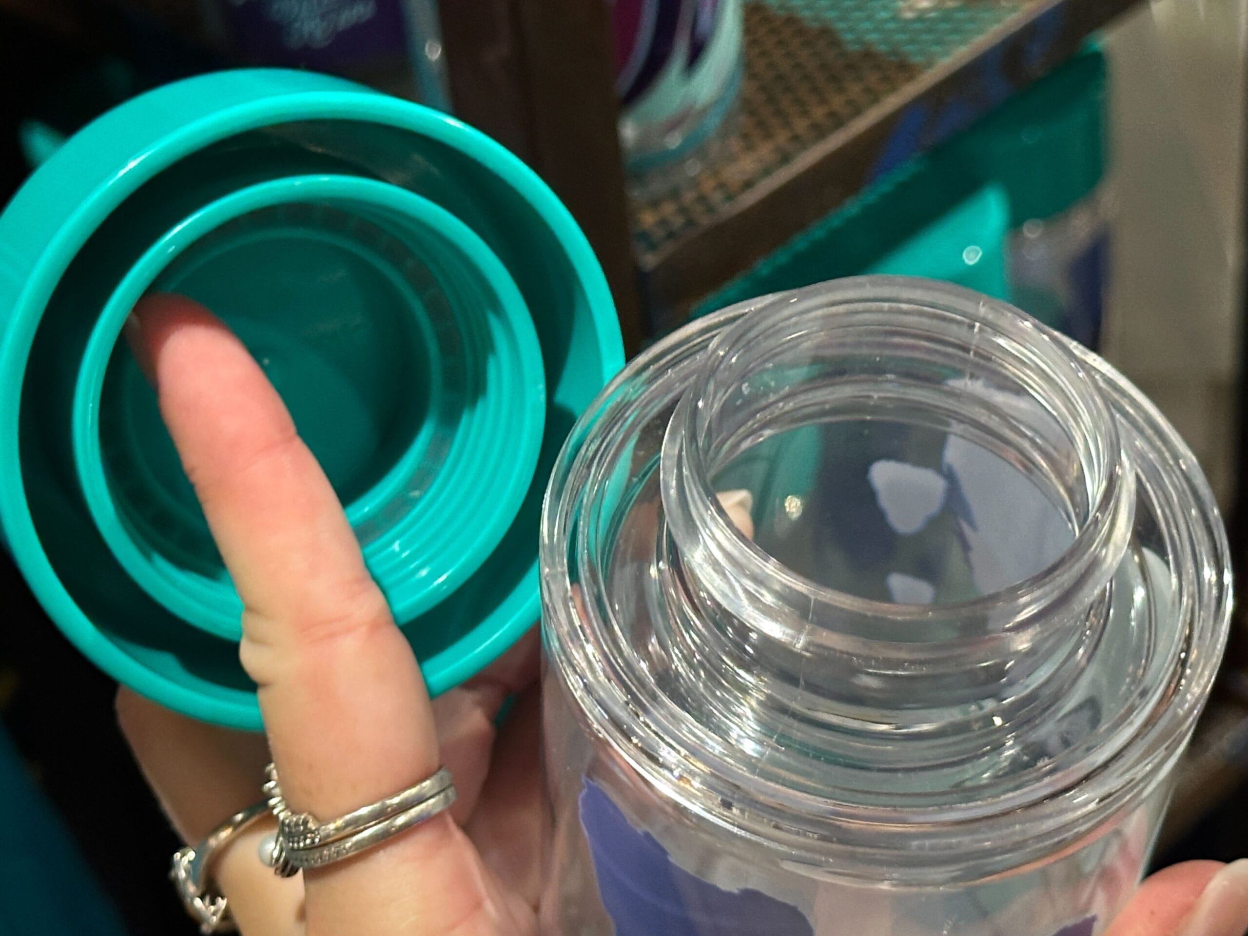A hand holding a turquoise Pandora Merch bottle lid beside a clear plastic bottle with a wide mouth opening.