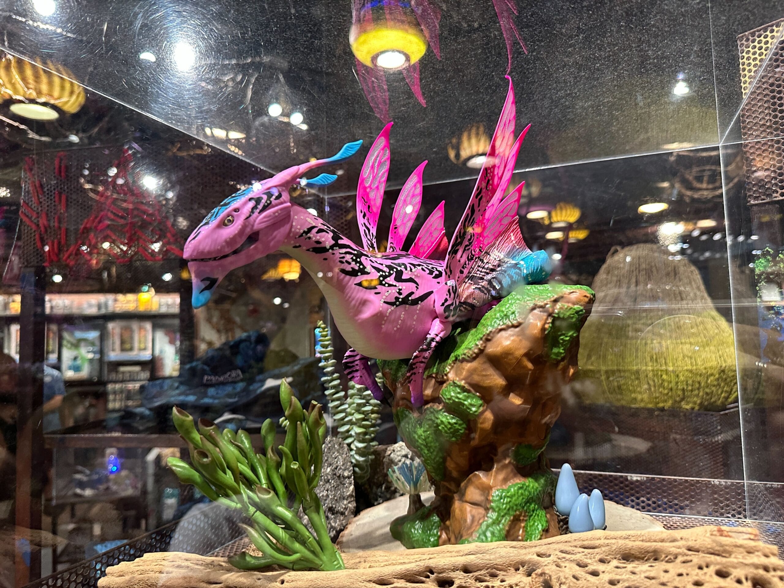 A Pandora dragon-like figurine with pink, blue, and purple wings sits on a rocky base inside a glass case.