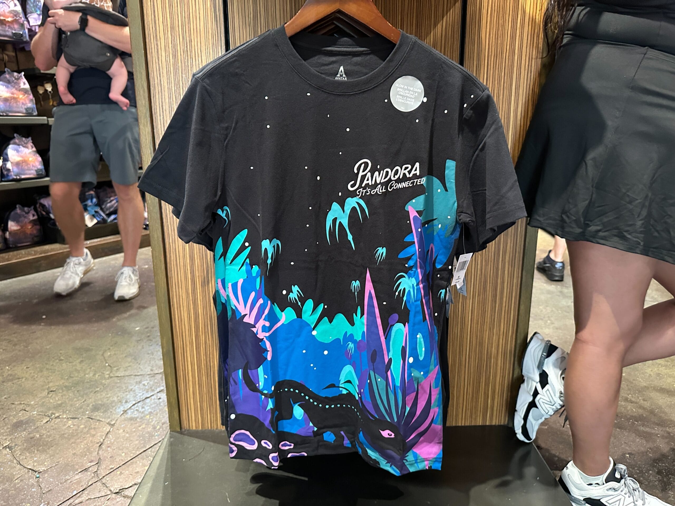 Black "Pandora: The World of Avatar" t-shirt, colorful alien landscape, perfect Pandora Merch on a wooden hanger.