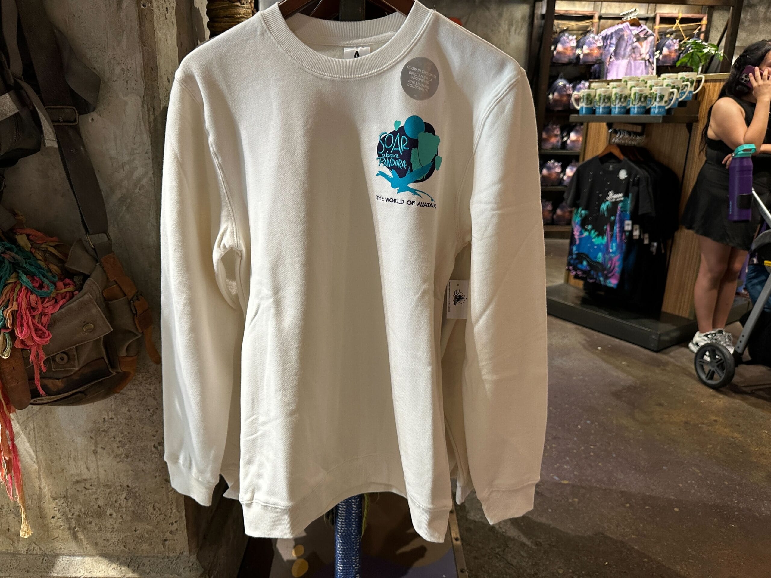 A white long-sleeve shirt with a blue Pandora design hangs on display among Avatar merchandise in a retail store.