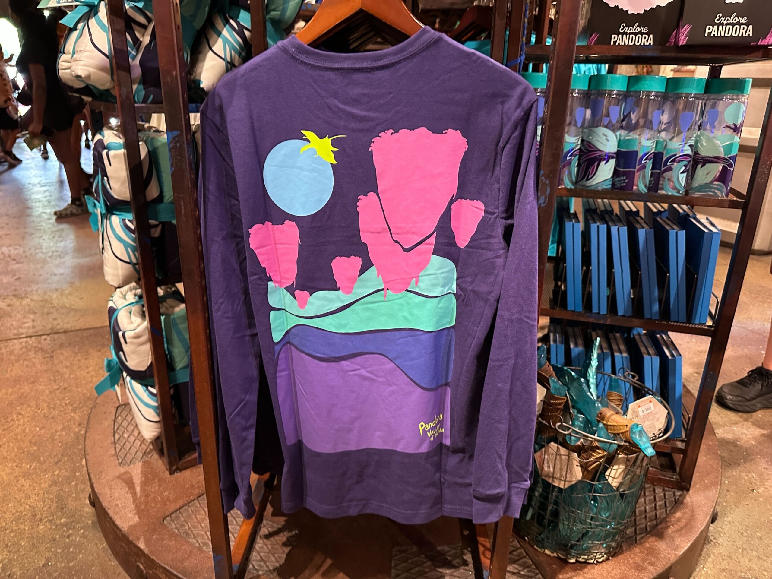A purple long-sleeve Pandora Merch shirt featuring a colorful abstract landscape and "Pandora" on the lower back.