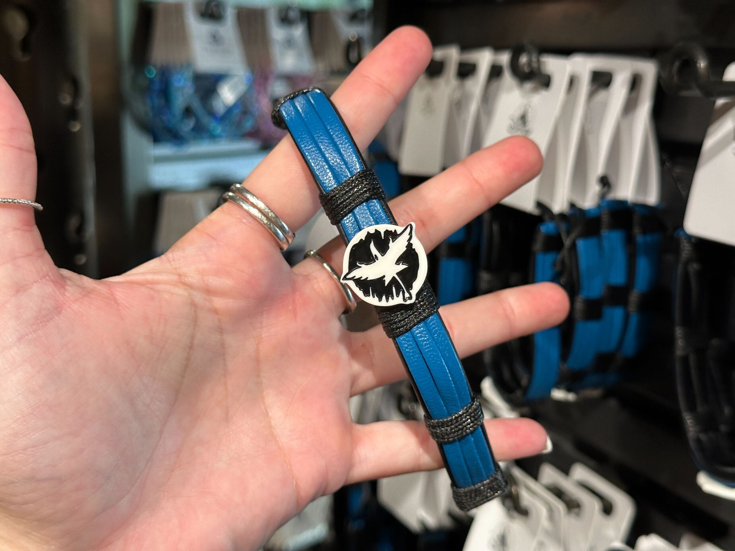 A hand holds a blue and black Pandora bracelet with a white lips and bat design; more bracelets hang in the background.