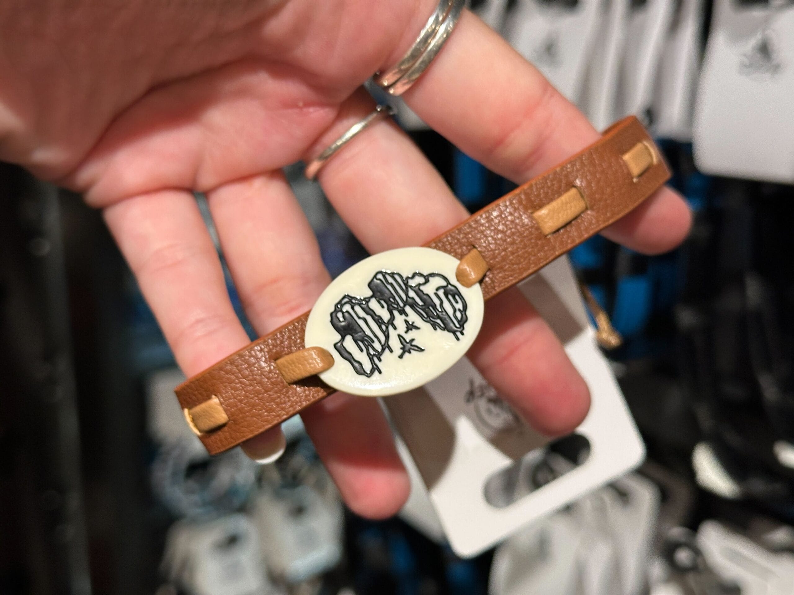 A hand holds a brown Pandora bracelet with a white oval charm featuring black dragon artwork.