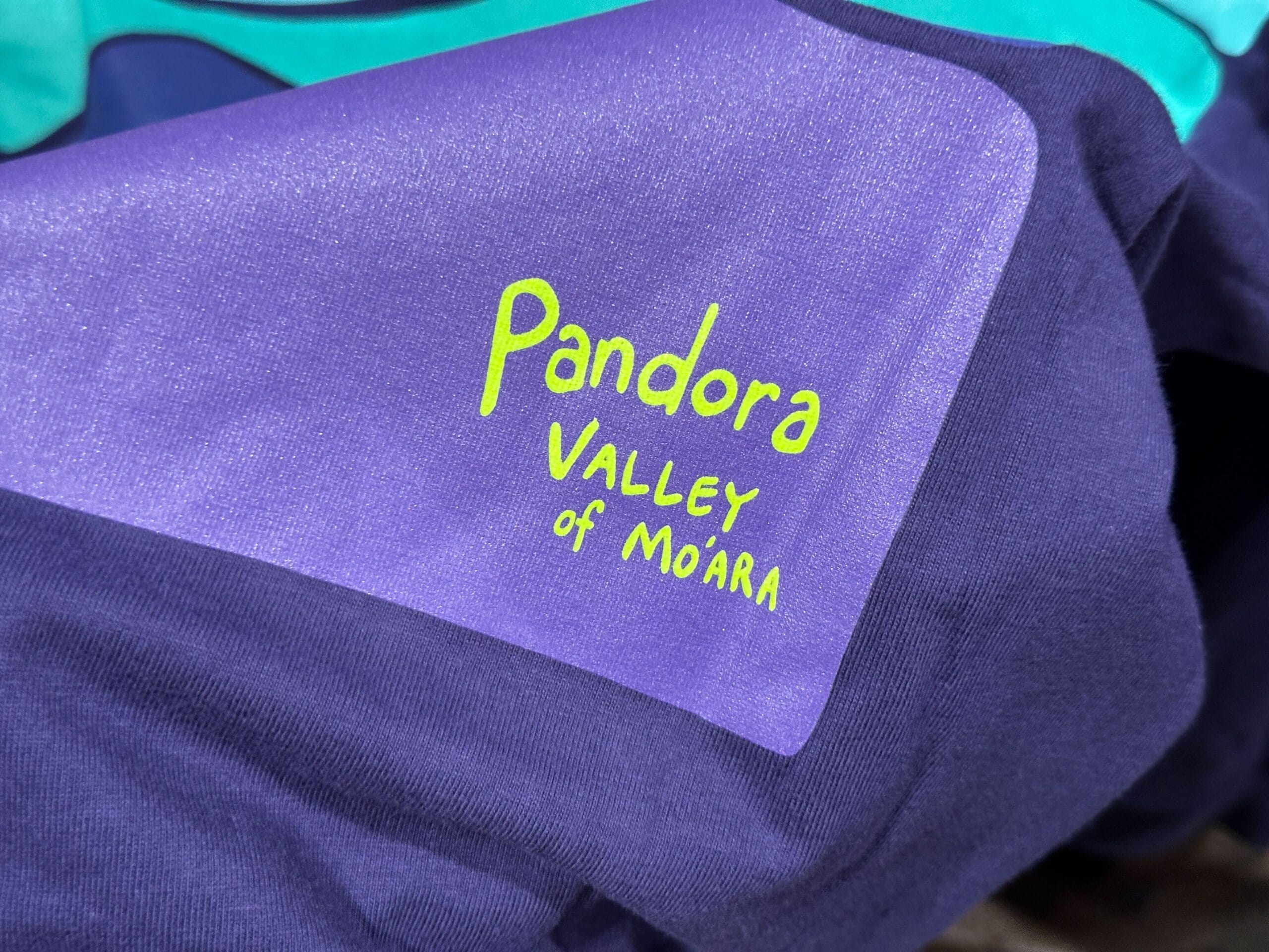Close-up of purple Pandora Merch fabric with yellow-green text reading "Pandora VALLEY of MO'ARA.
