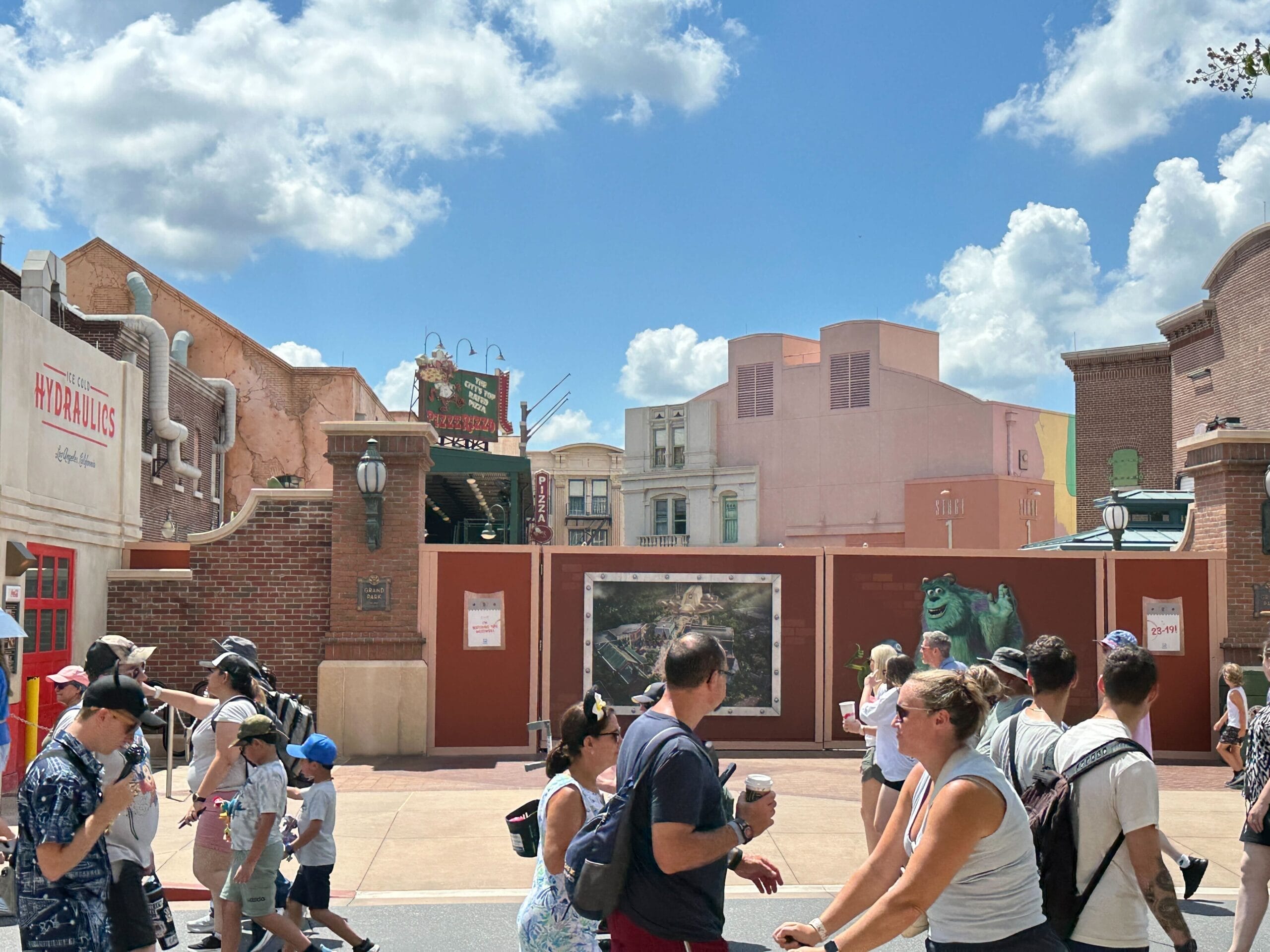 People walk past a construction wall for Monsters Inc. Land at Disney's Hollywood Studios on a sunny day.