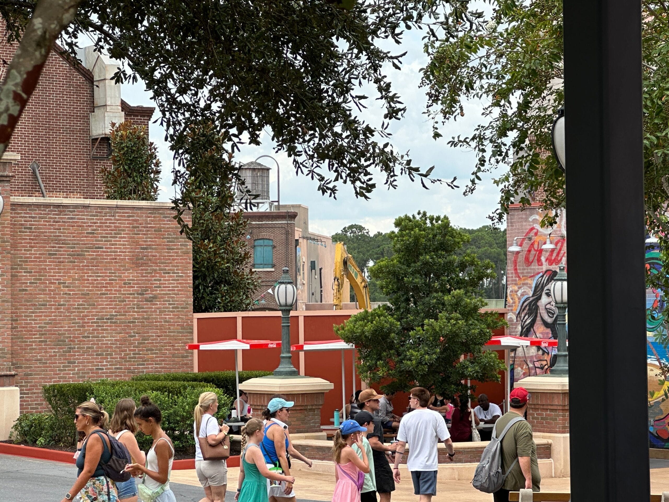 People walk past red construction walls near the Muppets Store at Disney's Hollywood Studios on a partly cloudy day.