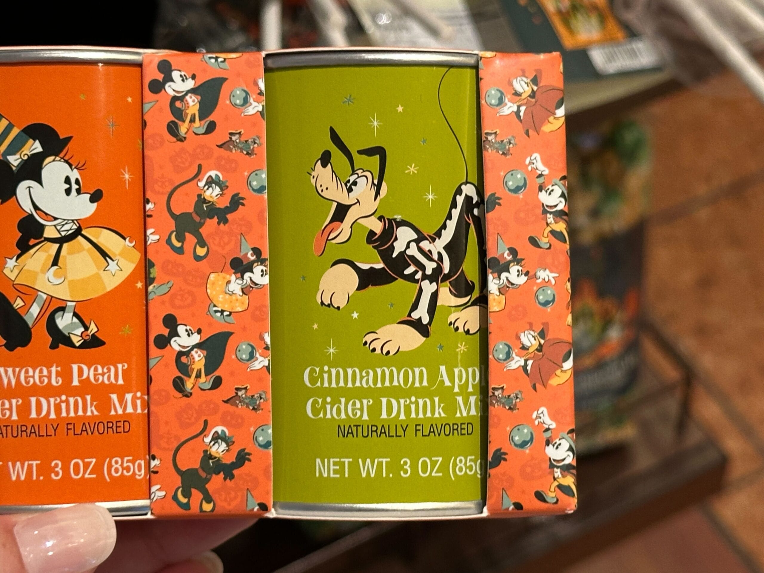 A tin of Cinnamon Apple Cider Drink Mix—Disney Halloween Merch 2025 featuring Pluto in costume on a green background.