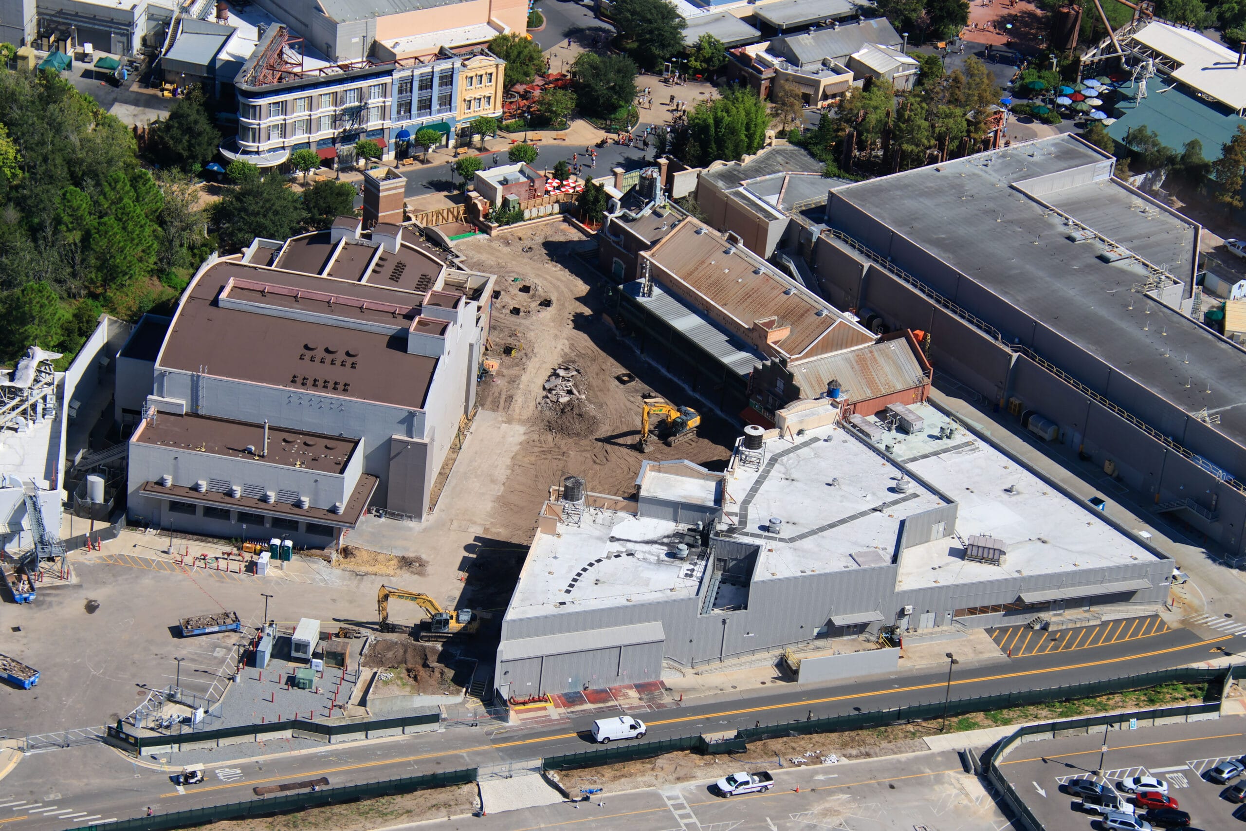 Aerial view of a construction site with flat dirt piles and equipment between large buildings.