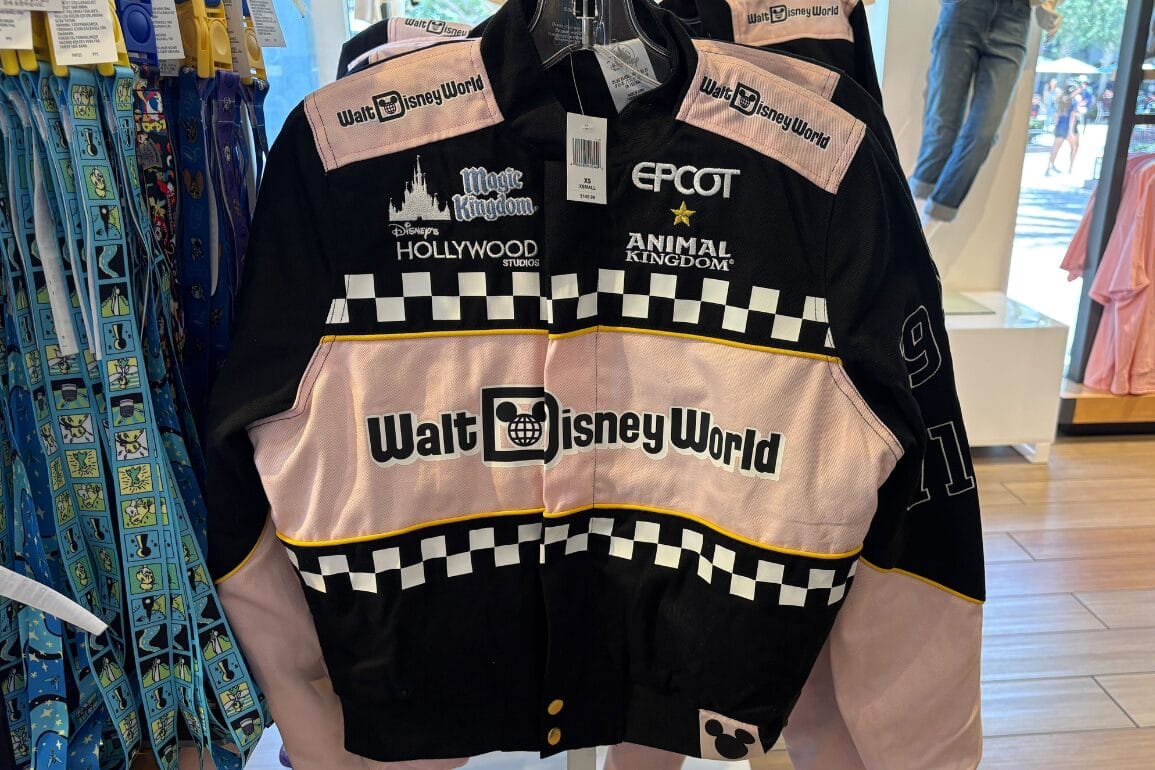 A Walt Disney World Racing Jacket with park logos and pink sleeves hangs in a Disney Springs store.