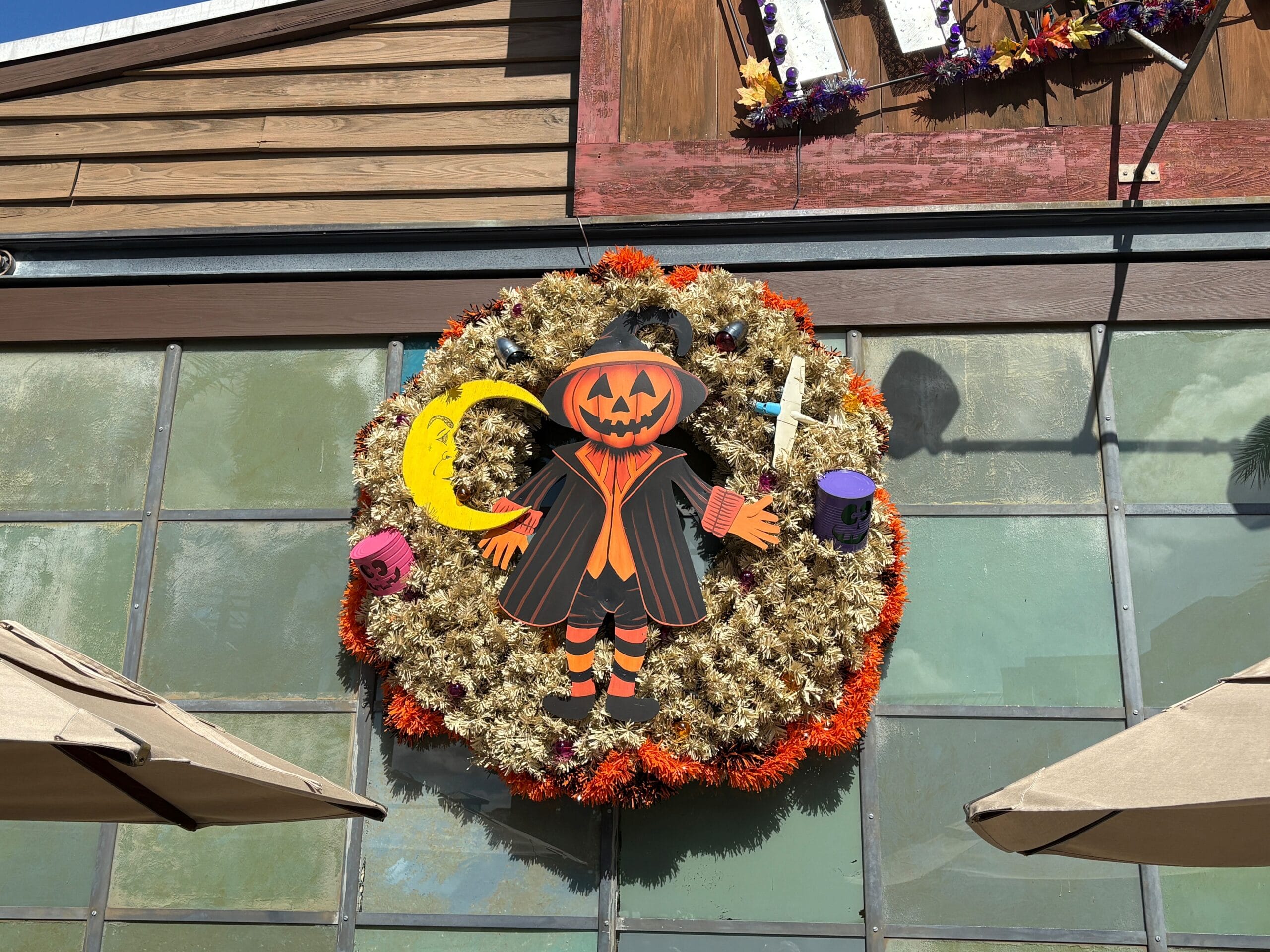A Halloween overlay wreath with a pumpkin-headed figure and candles hangs above windows at Disney Springs.