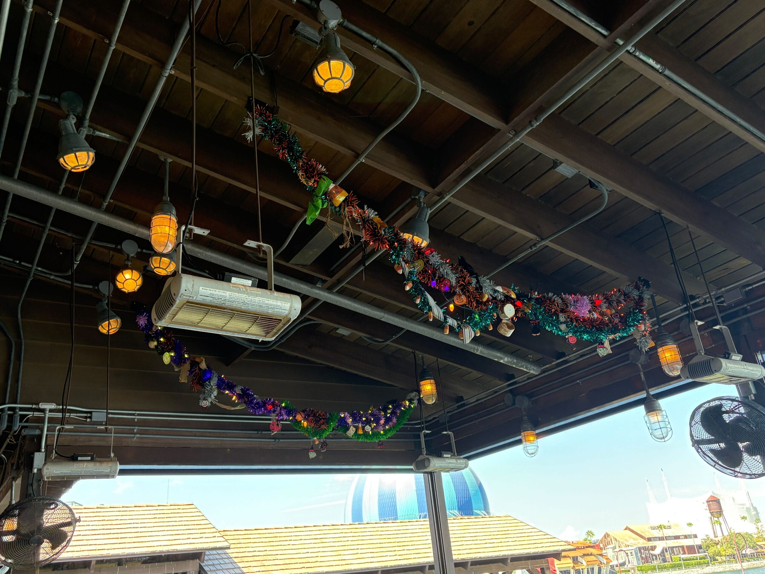 Colorful tinsel garlands and ornaments hang at Jock Lindsey's Hangar Bar in Disney Springs, framed by string lights and pipes.