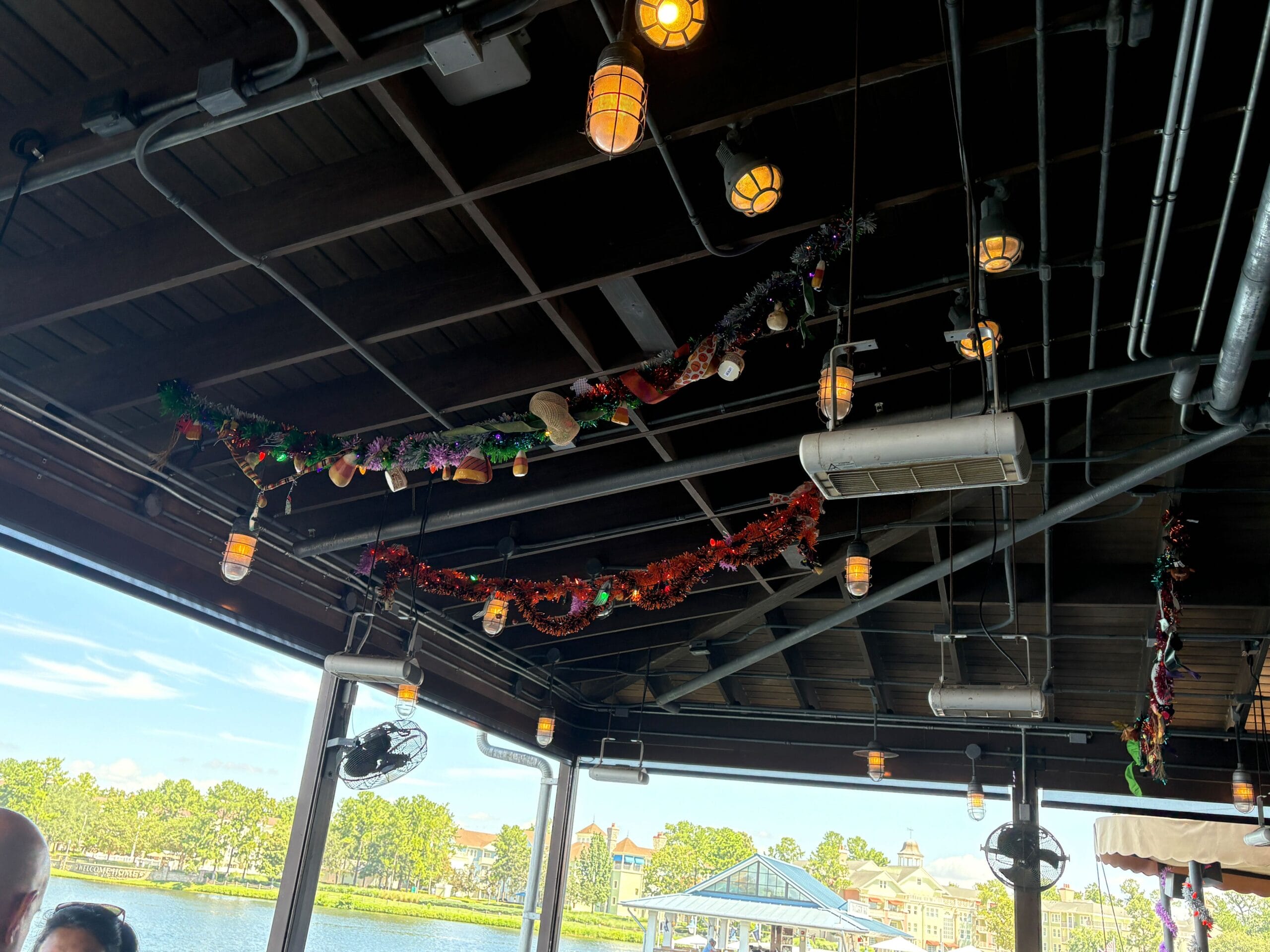 Colorful holiday garland hangs at Disney Springs' Jock Lindsey's Hangar Bar, with a Halloween overlay and lake views.