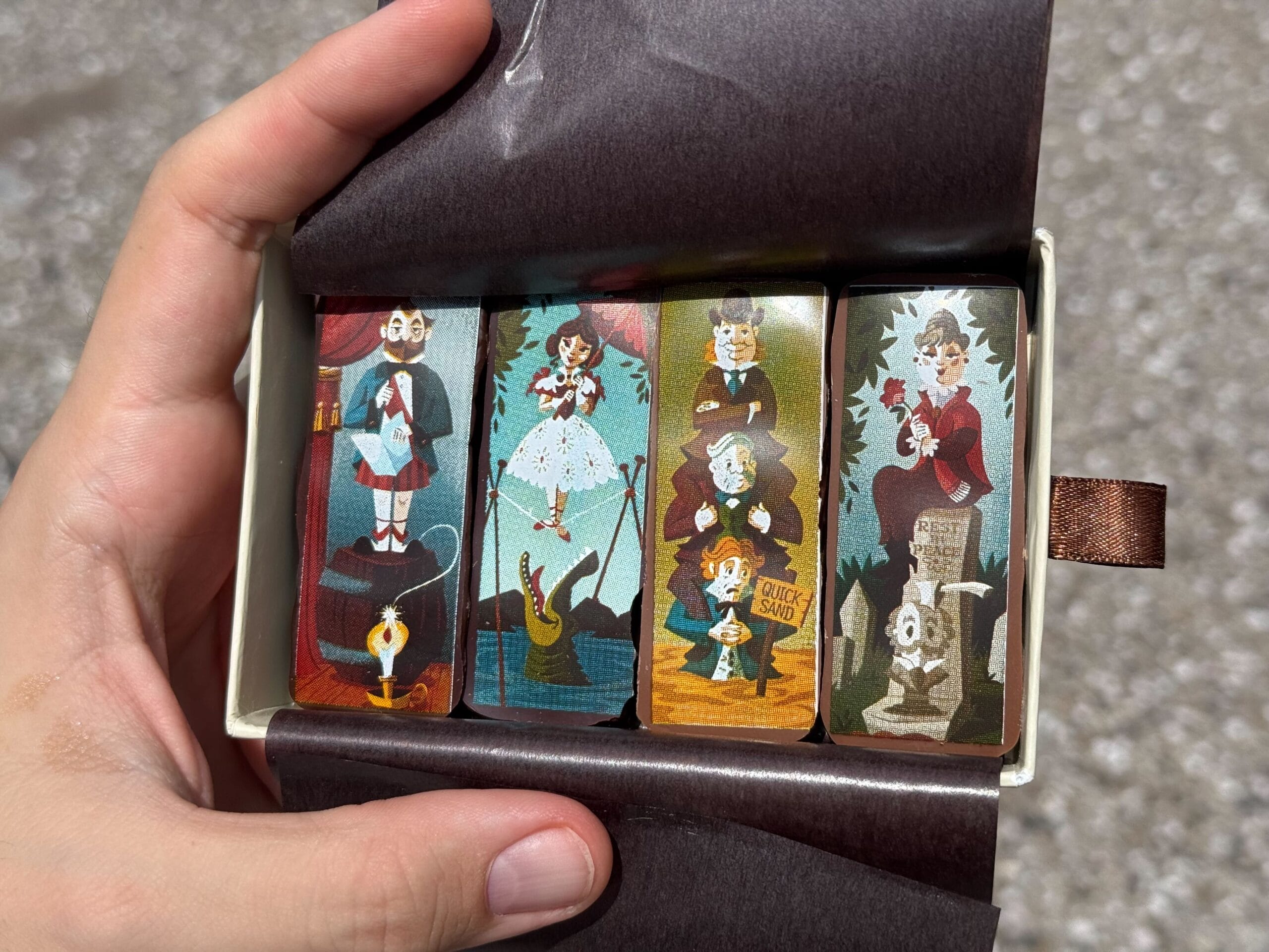 A hand holds a box of four illustrated lipsticks with haunted mansion themed designs at Disney Springs.