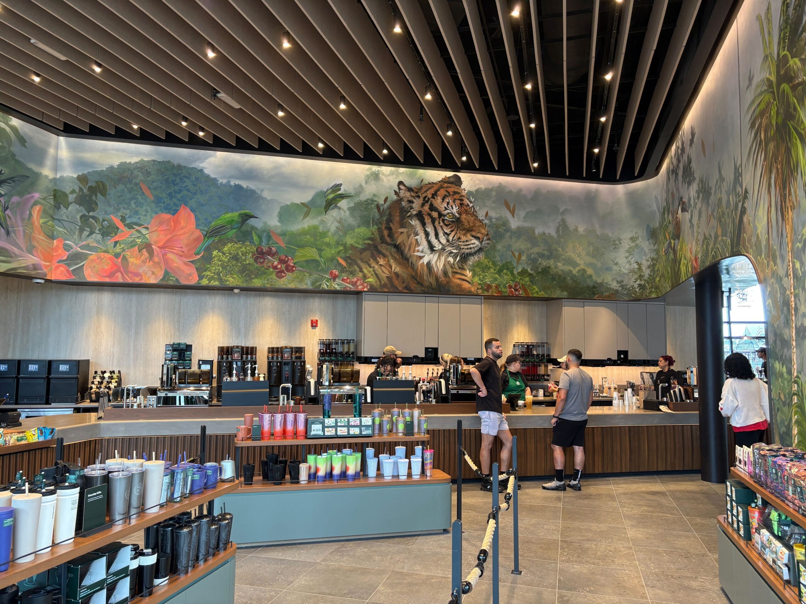 People order drinks at a modern café in Disney Springs, with a mural of a tiger and jungle scene above the counter.