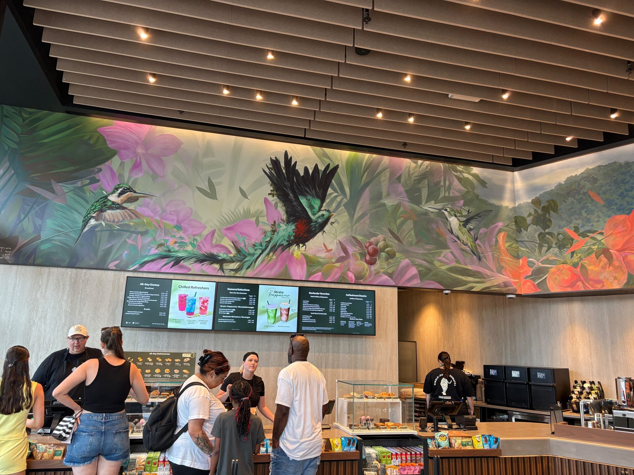 Customers order at a Starbucks café counter in Disney Springs, where a vibrant mural brightens the newly reopened space.