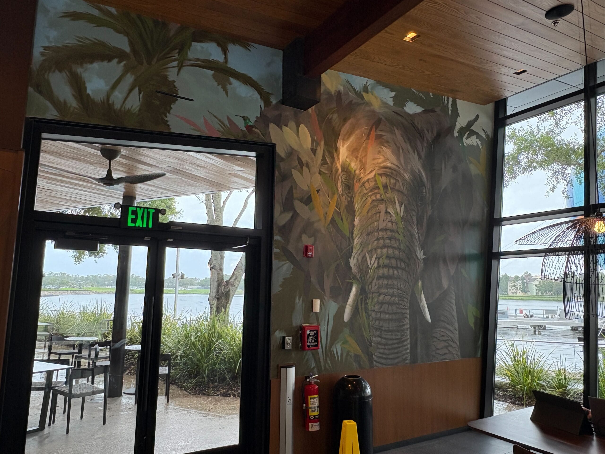 A mural of an elephant and jungle plants decorates a refurbished restaurant wall near windows overlooking Disney Springs.
