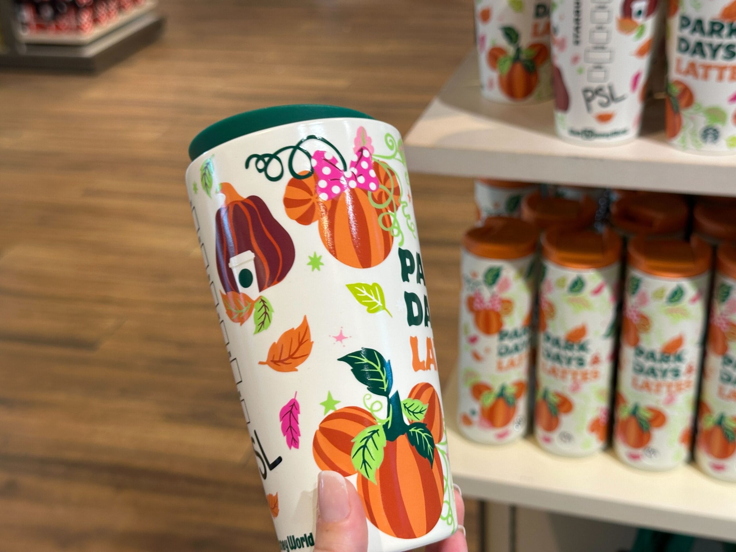 Hand holds a colorful travel mug with pumpkins, perfect for Disney Parks or your Starbucks Pumpkin Spice fix.