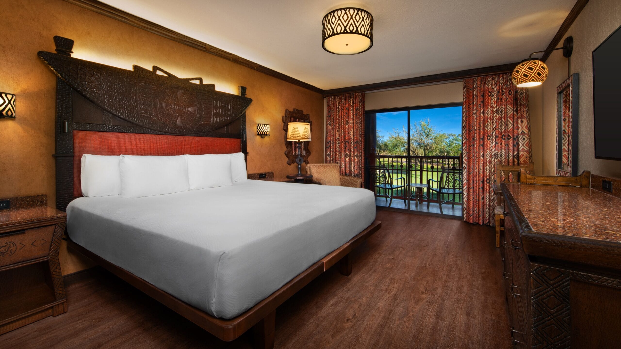 Refurbished guest room at Disney's Animal Kingdom Lodge with a large bed, tribal decor, desk, and balcony among the trees.