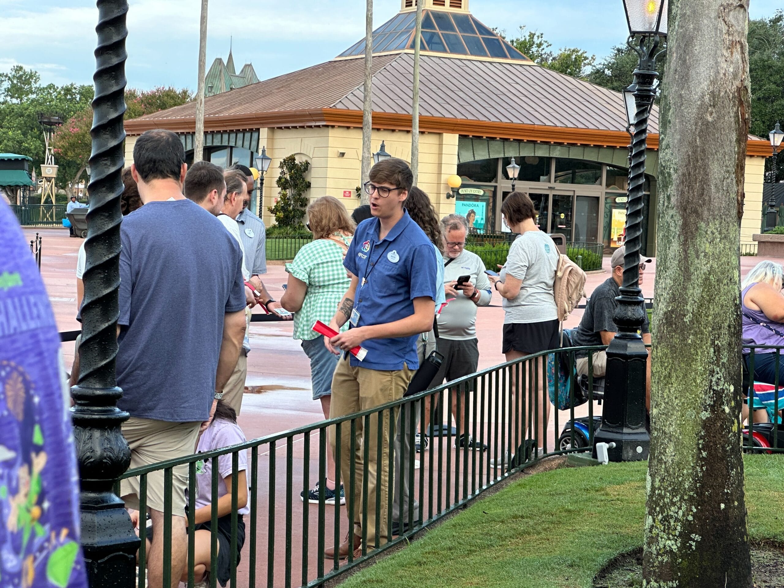 A theme park employee hands out wristbands in line about the latest pin release near a building on a cloudy day.