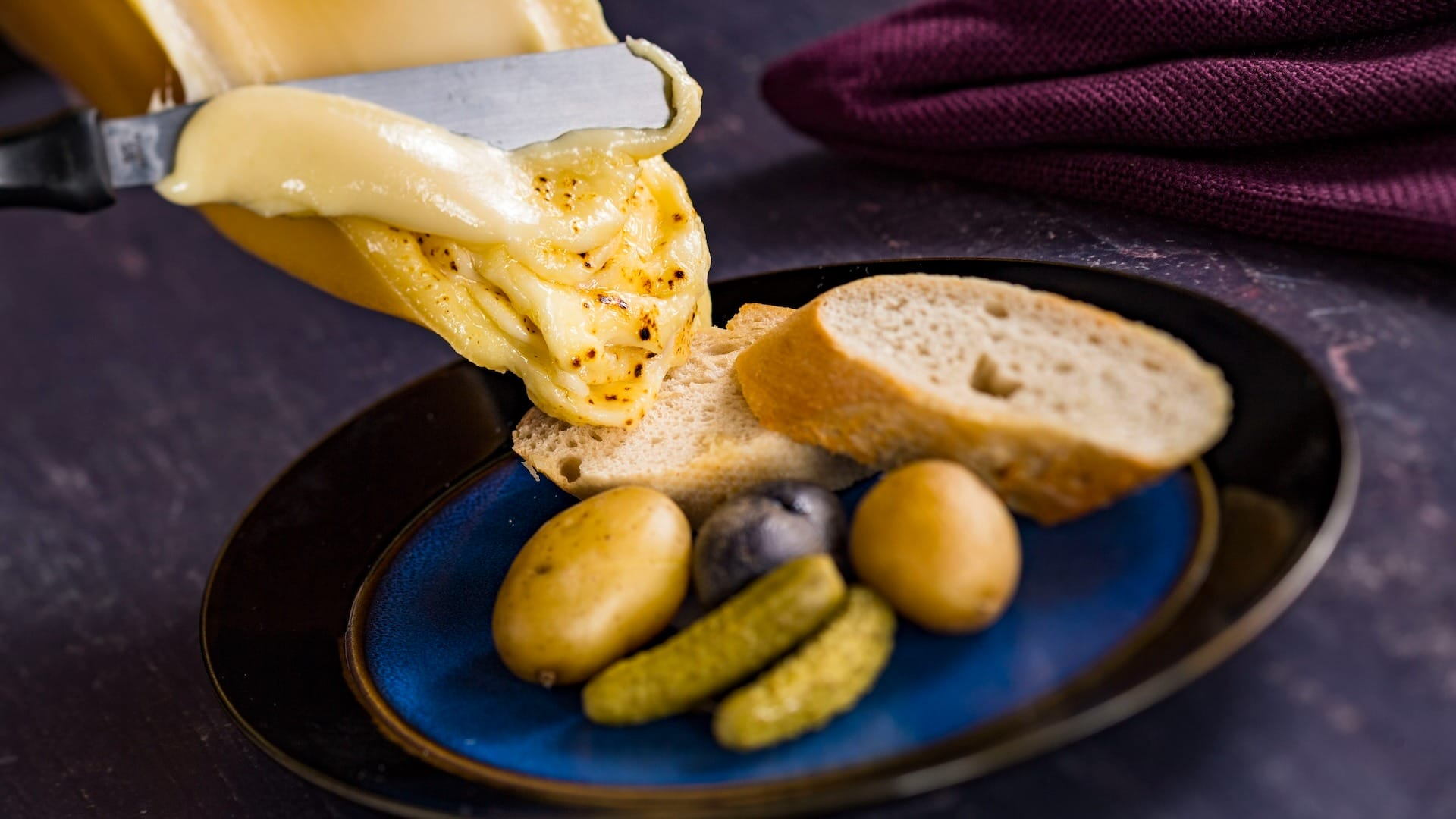 Melted cheese scraped onto bread, with potatoes and pickles—discover it on EPCOT Food & Wine Festival 2025 menus.