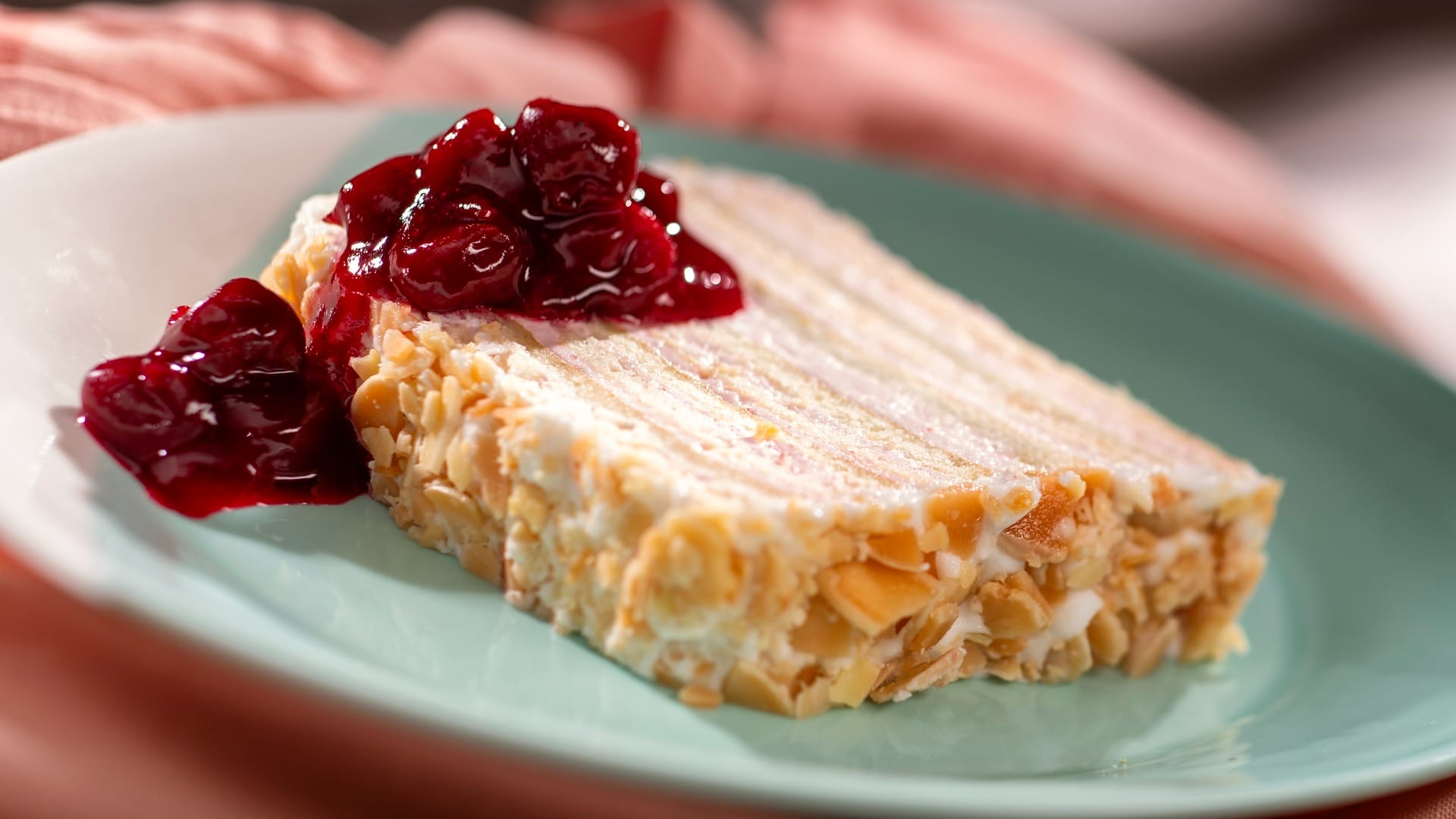 A slice of layered cake with cream and almonds, perfect for EPCOT Food & Wine Festival 2025 menus, on a green plate.