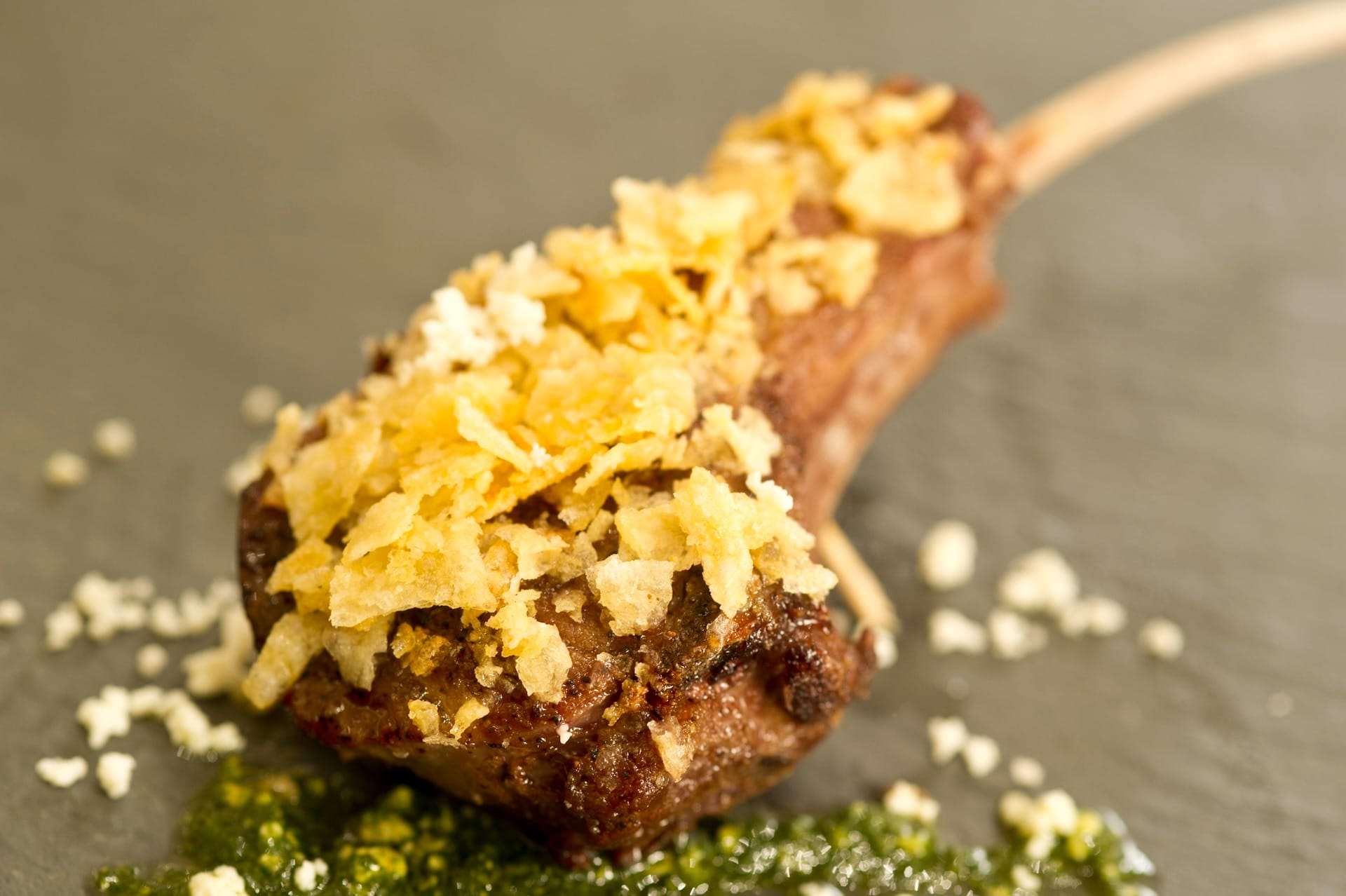A lamb chop topped with crushed potato chips and green sauce, featured on 2025 menus at the EPCOT Food & Wine Festival.