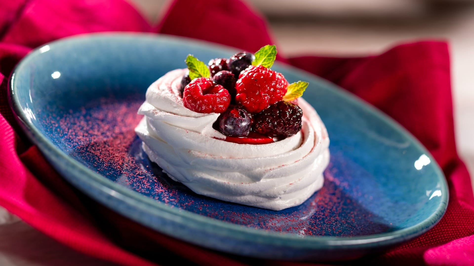 A meringue dessert from the EPCOT Food & Wine Festival 2025, topped with berries and mint on a blue plate with red cloth.