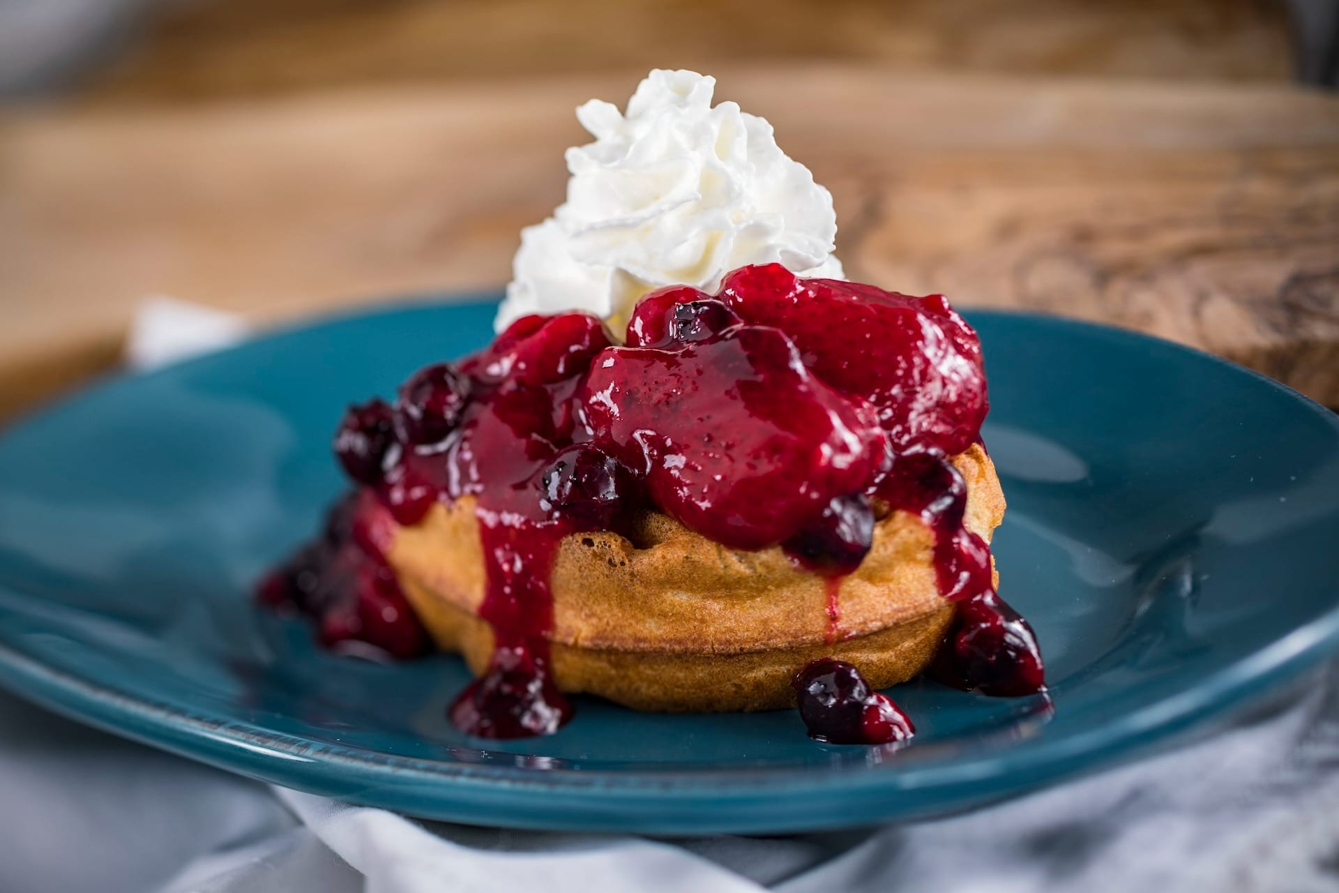 A waffle topped with berry sauce and whipped cream, inspired by the EPCOT Food & Wine Festival, on a blue plate.