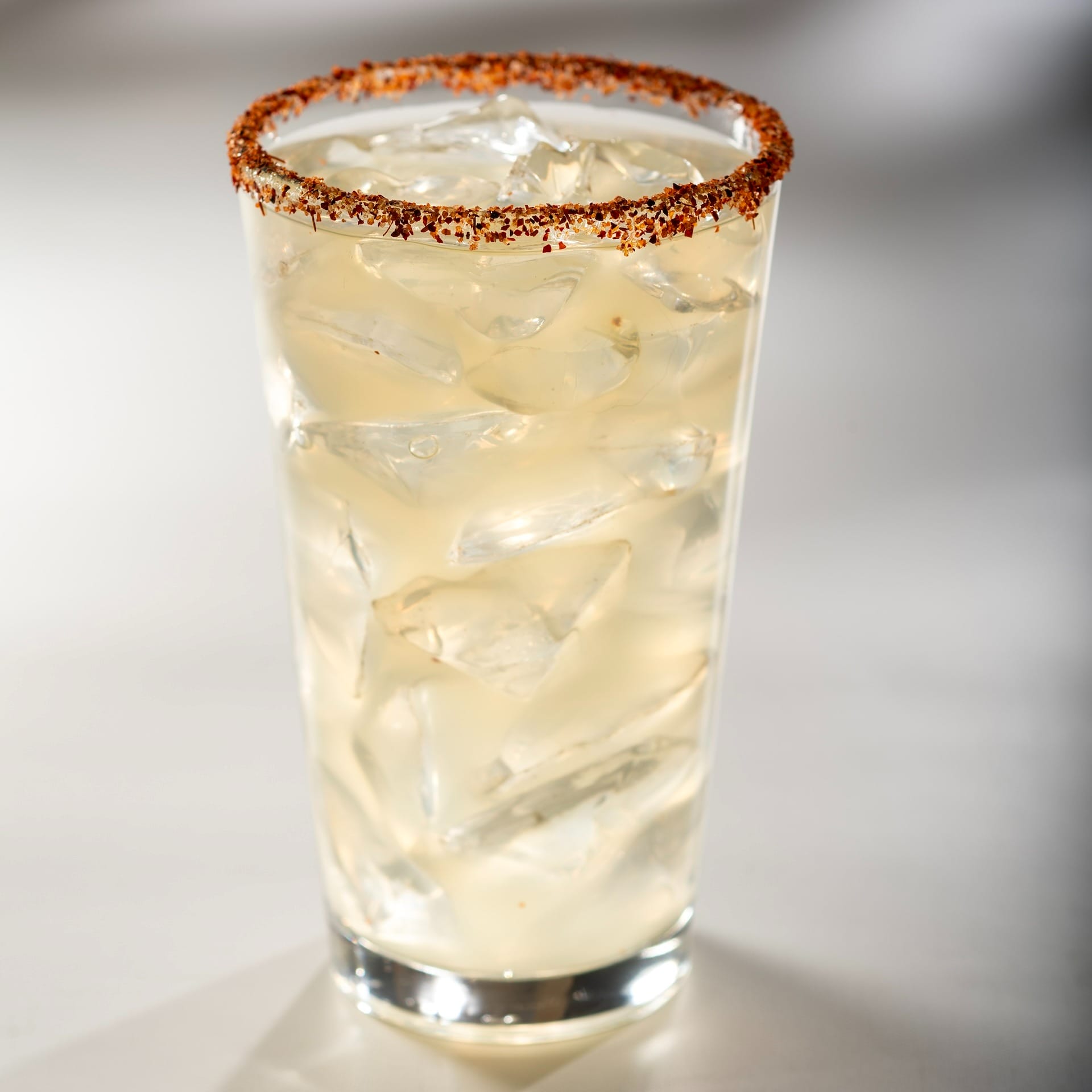 A glass of iced beverage with a chili powder rim, inspired by EPCOT Food & Wine Festival, on a white surface.
