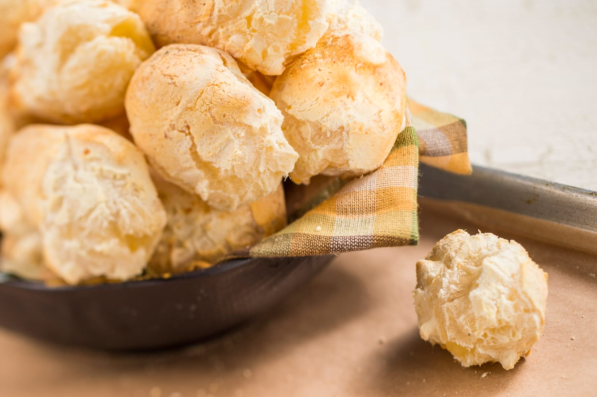 A bowl of Brazilian cheese bread rolls at EPCOT Food & Wine Festival 2025, with one on a baking tray nearby.