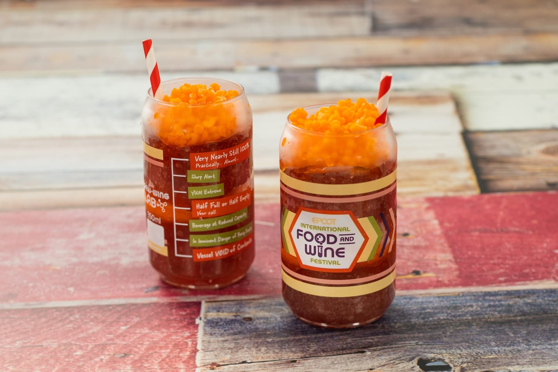 Two drinks in jars with red straws, orange boba, and EPCOT Food & Wine Festival 2025 menus on a rustic wooden table.