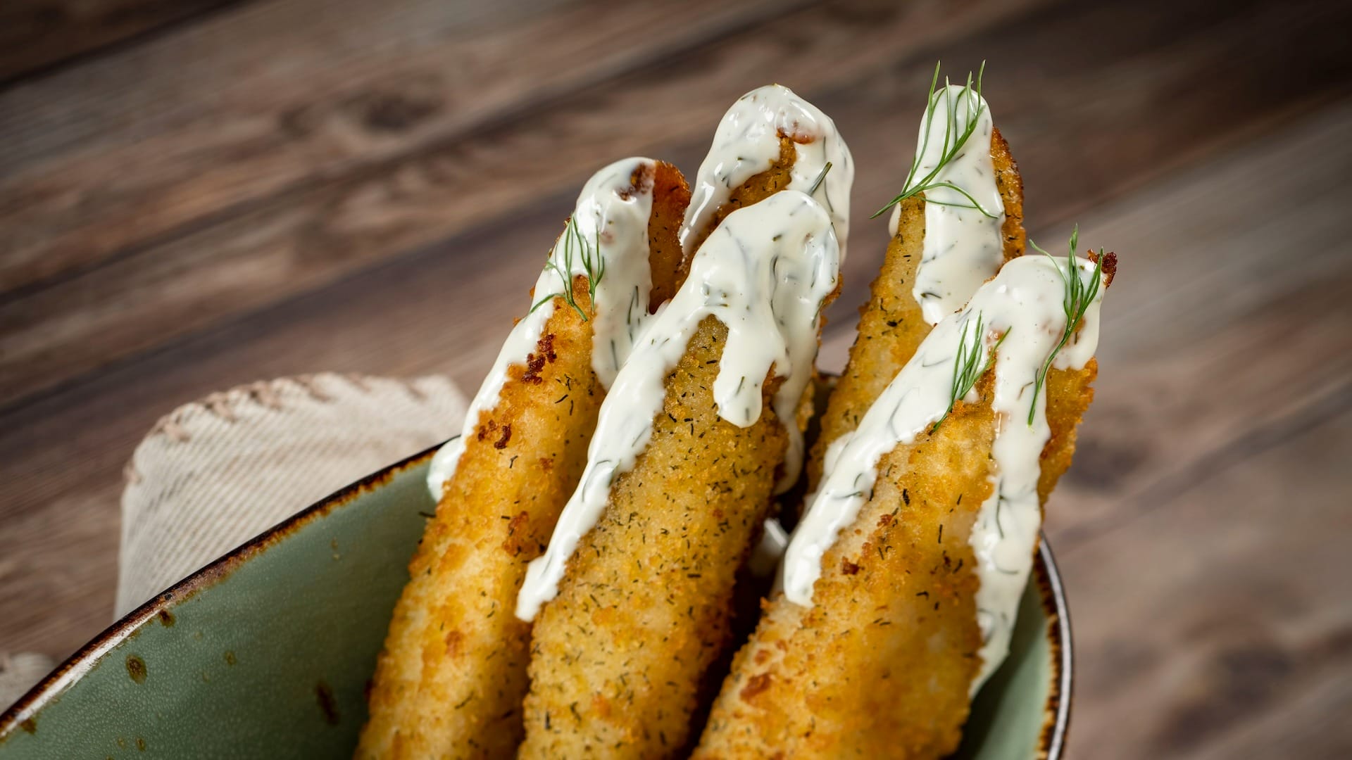 Three breaded fried fish fillets with creamy sauce and dill, inspired by EPCOT Food & Wine Festival, in a green bowl.
