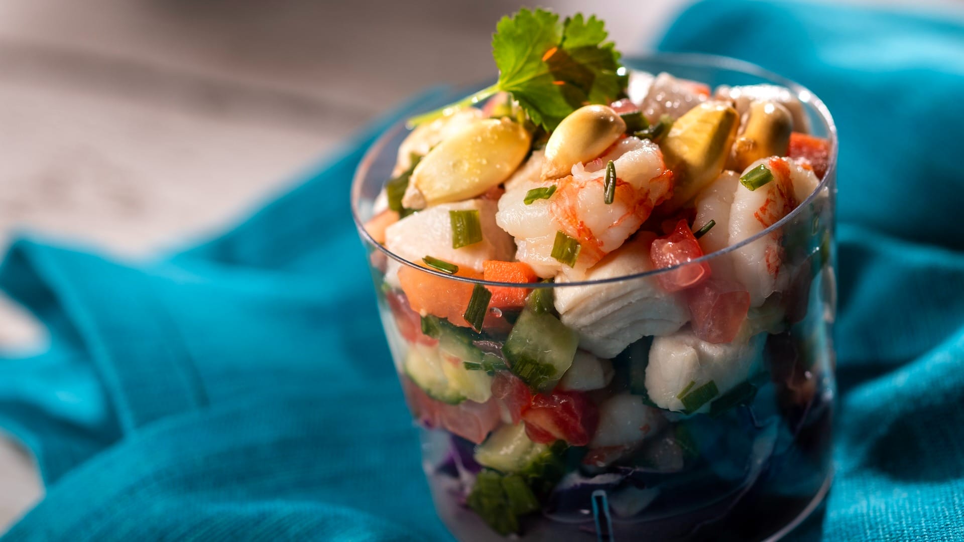 A glass of ceviche, garnished with cilantro and corn nuts, shines at the EPCOT Food & Wine Festival on a blue cloth.