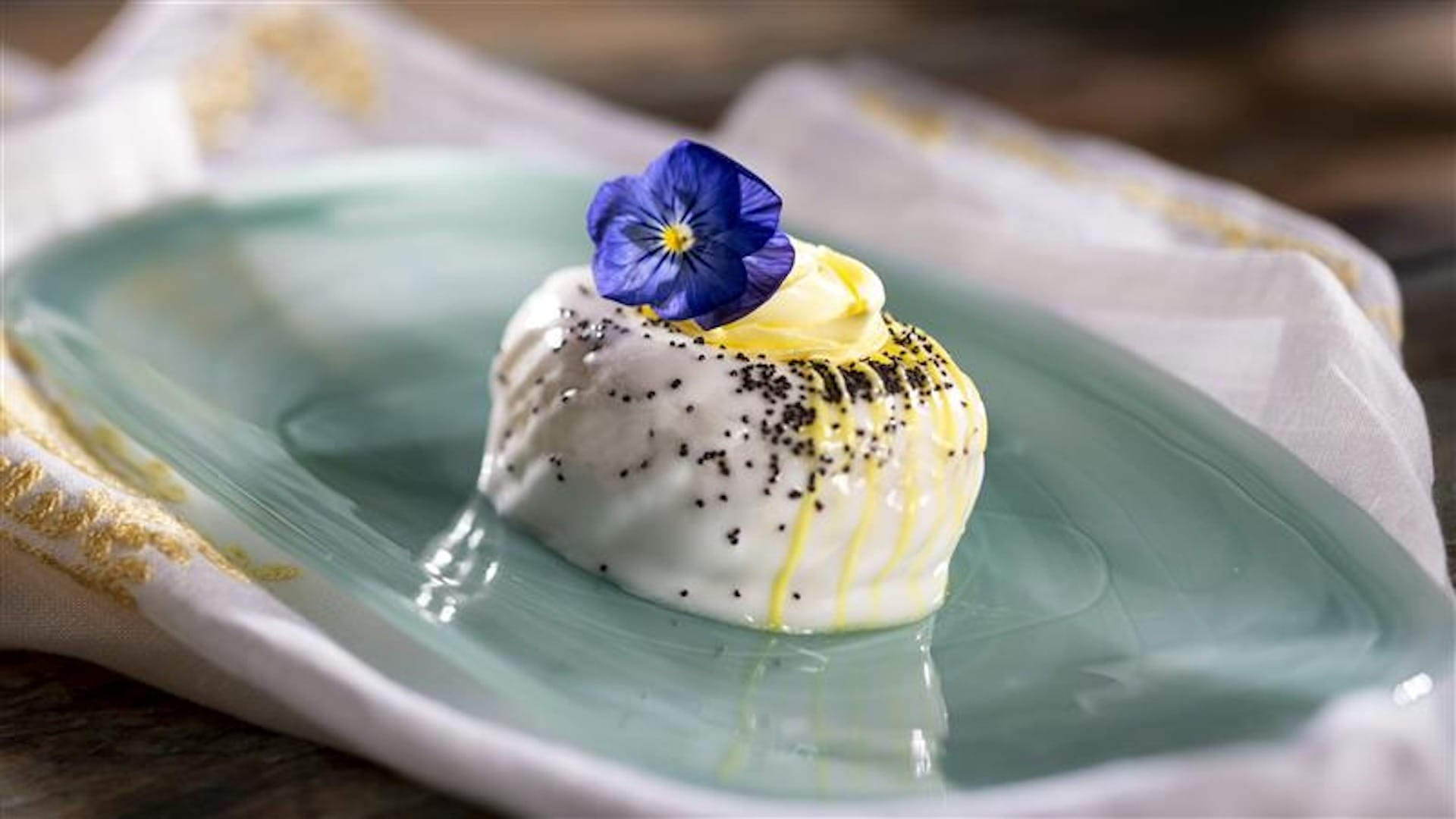 Elegant dessert covered in white icing, topped with a purple flower and poppy seeds—perfect for the EPCOT Food & Wine Festival.